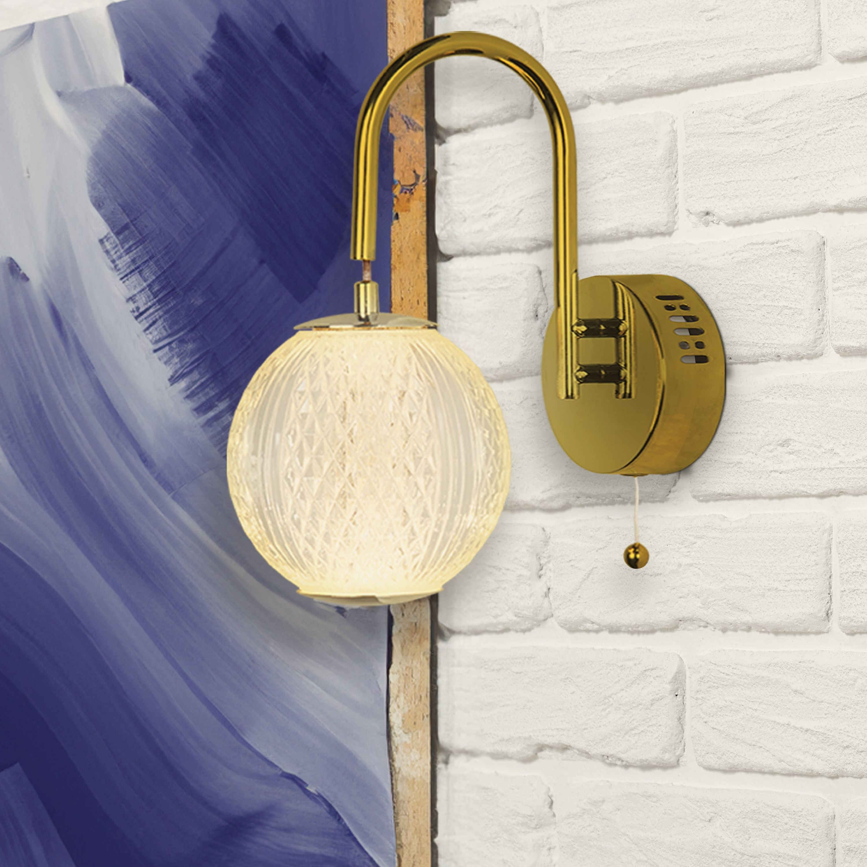 Allure wall light in satin brass mounted on a brick wall beside an abstract painting, globe lit with a warm glow