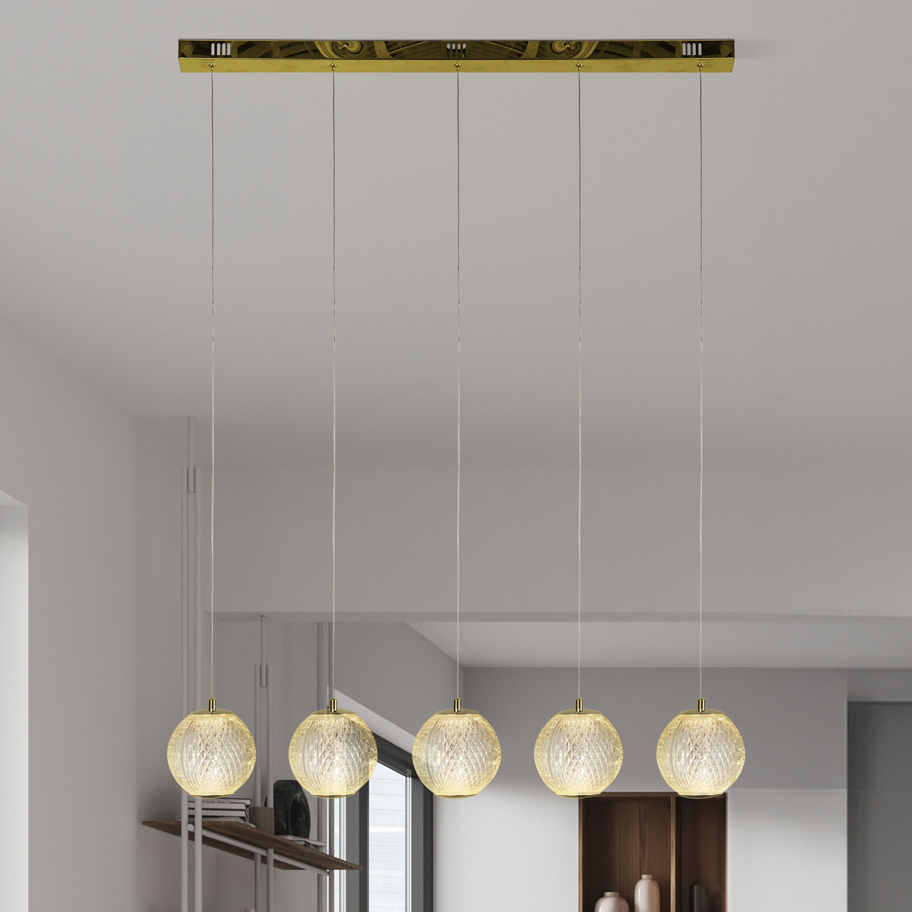 Allure 5 light bar pendant in satin brass styled above a console table in a living space, globes lit with a warm glow