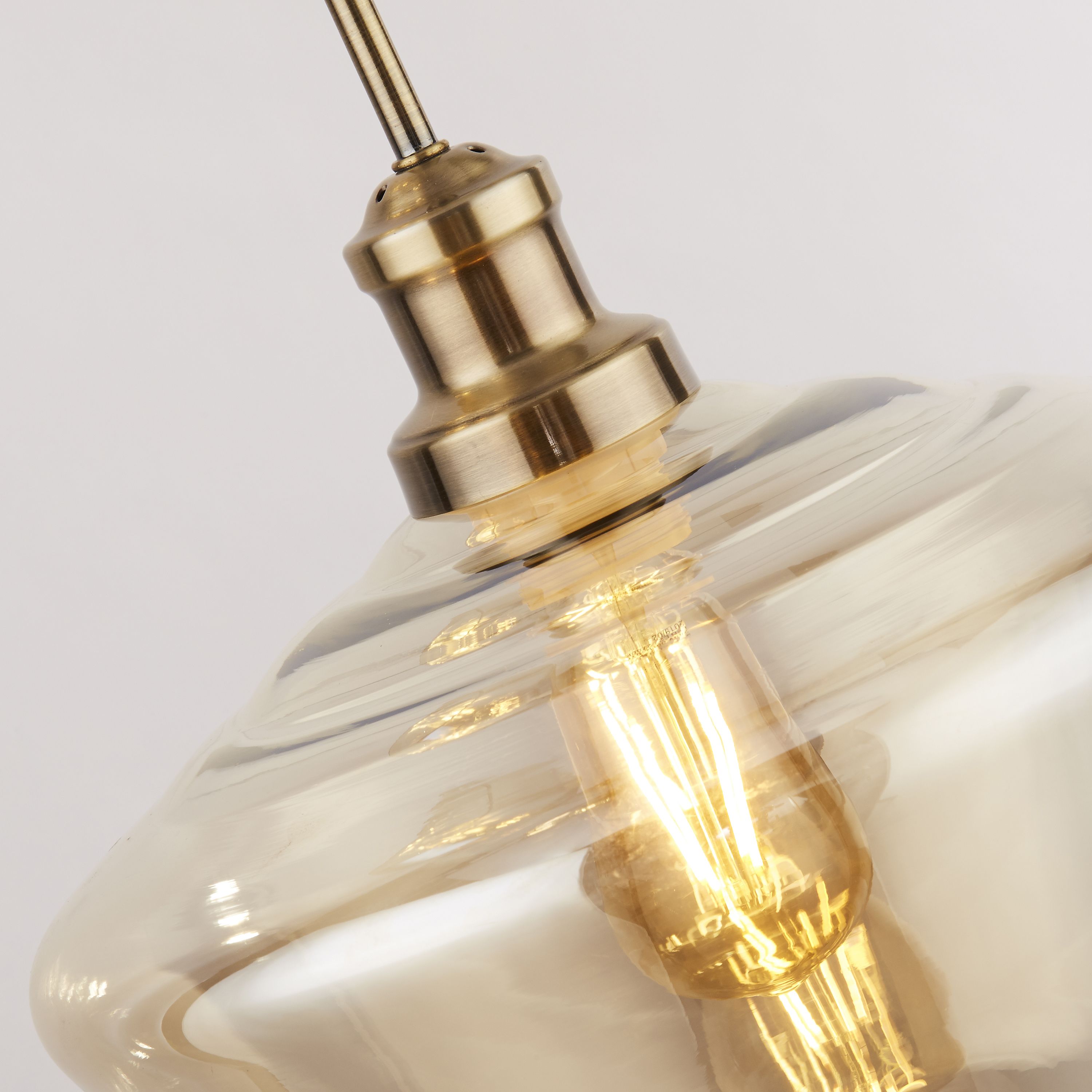 Close up of the Searchlight Mia pendant showing the antique brass lampholder and ribbed amber glass shade with a lit filament style bulb inside