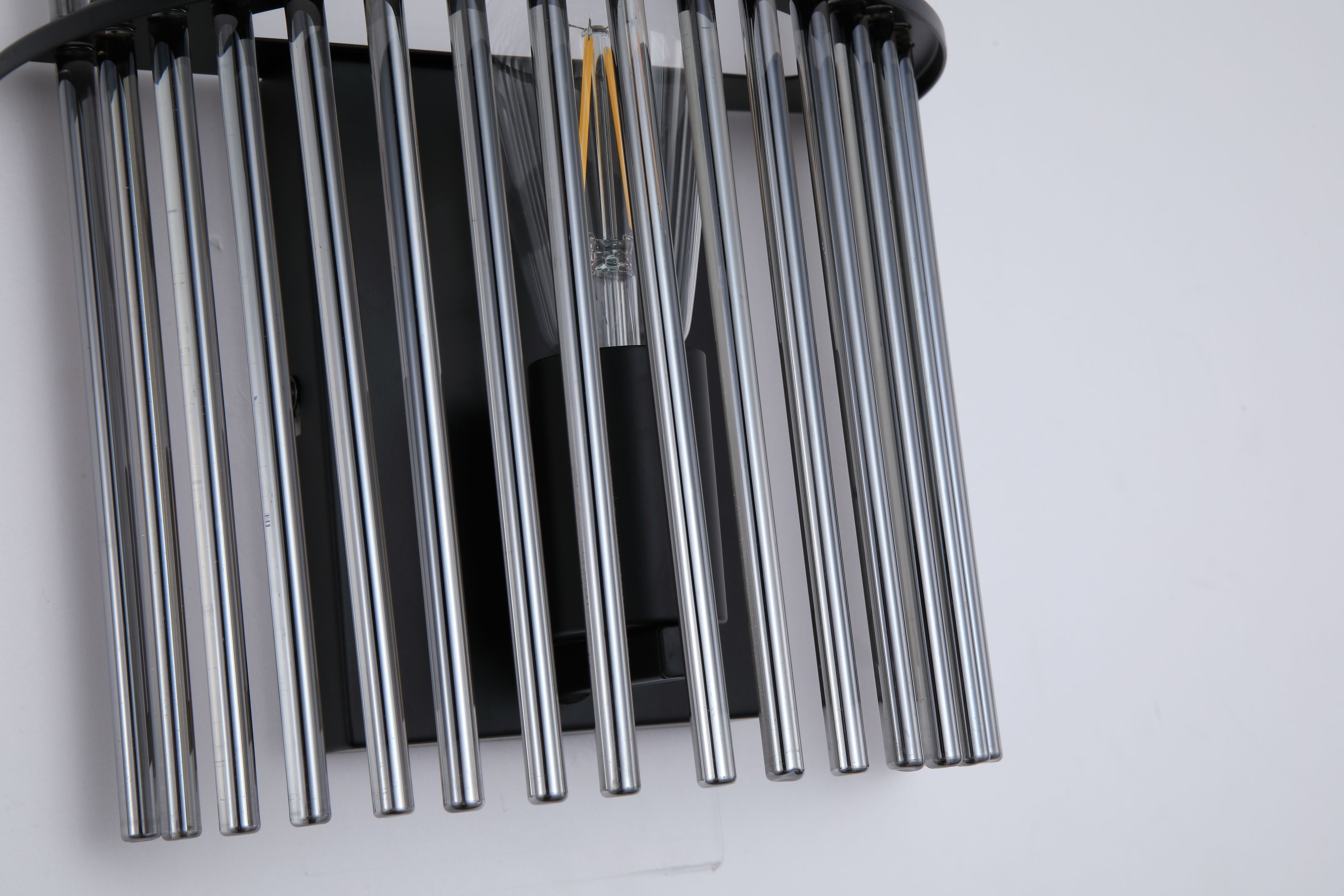 Close up from above of the Swizzle wall light, smoked glass rods around the lit E27 bulb and black backplate
