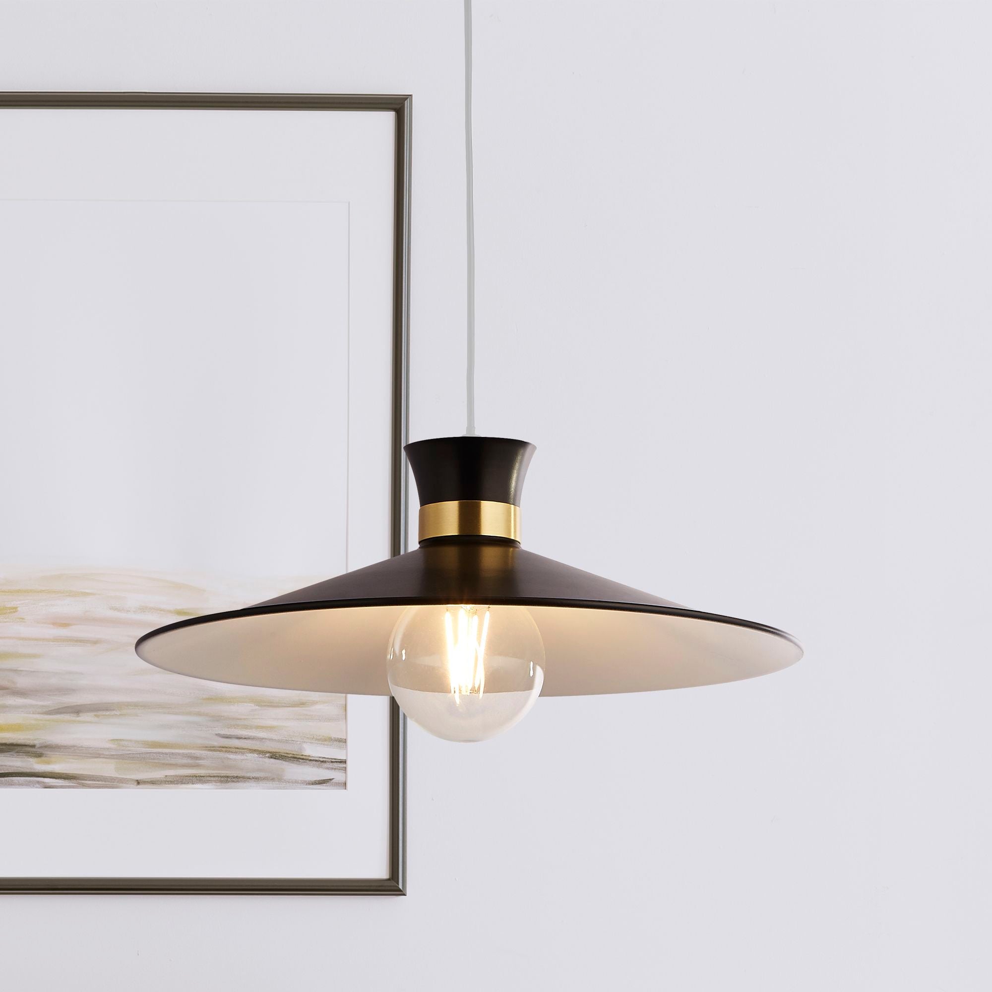 Searchlight Balham pendant light styled near a framed piece of art, matt black and brass shade with a softly lit bulb