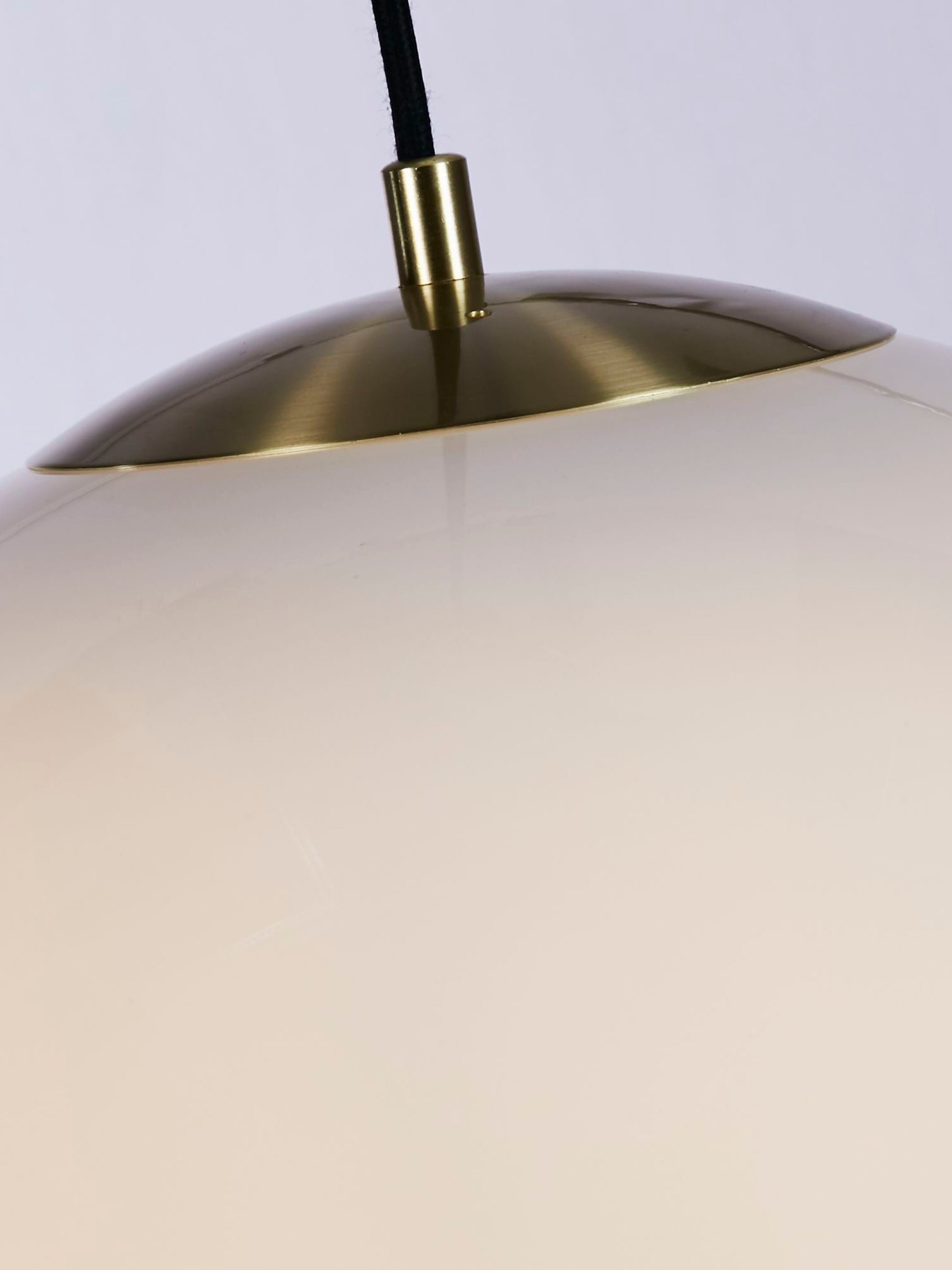 Close up of the Atom pendant's fitting, showing the brass toned lamp holder set into the opal glass globe with a black cable running down