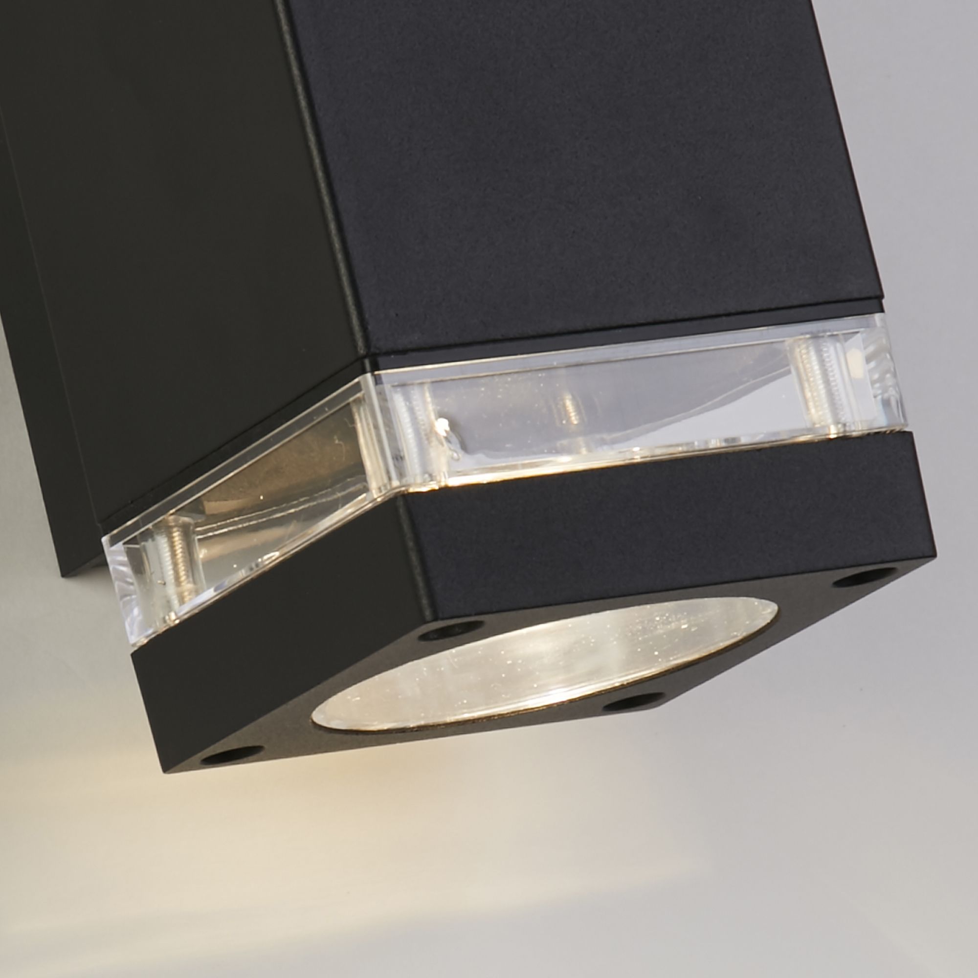 Close up of the Houston black wall light's clear lens and corner fixing screws, showing the matte black aluminium finish in detail