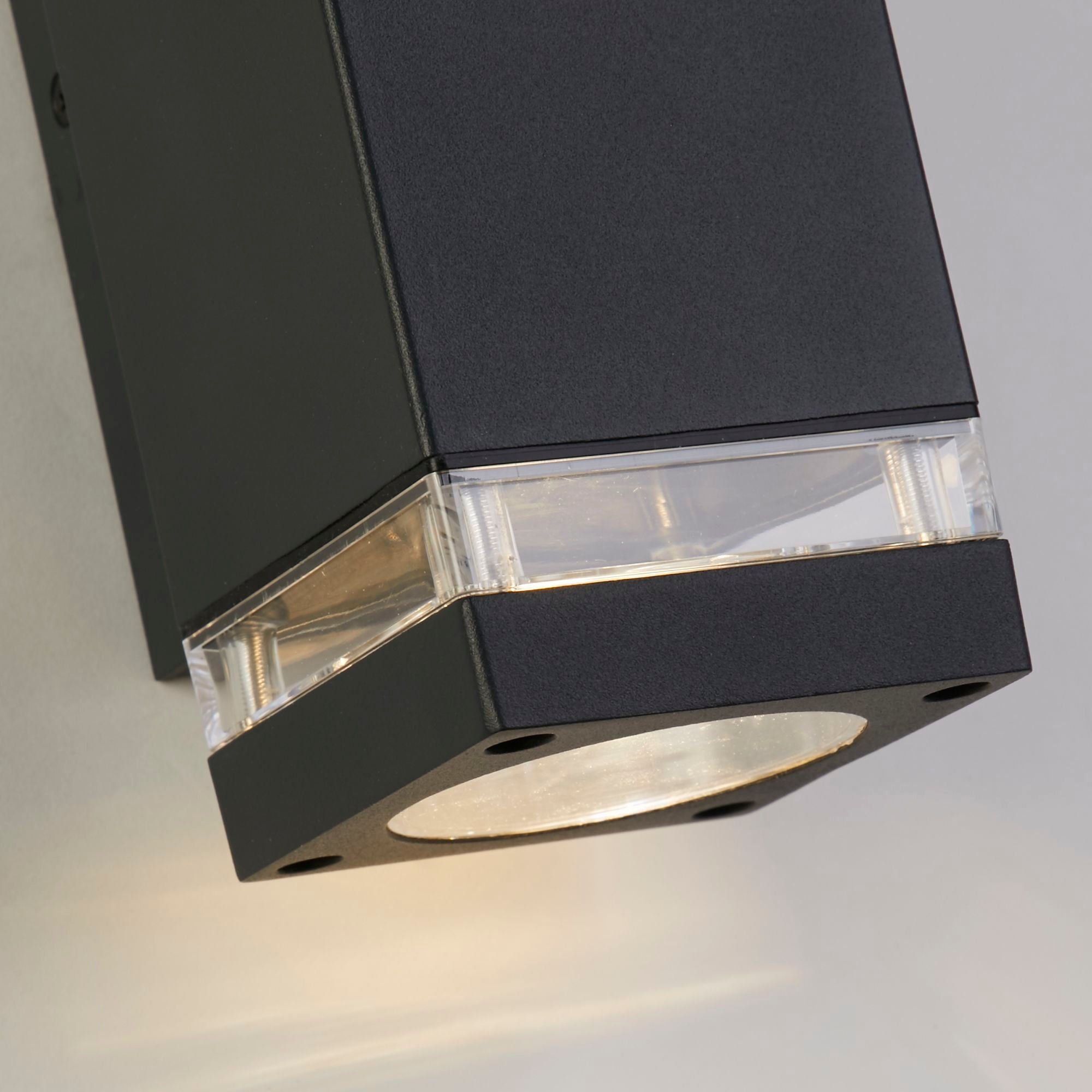 Close up of the Houston grey wall light's clear lens and corner fixing screws, showing the graphite grey aluminium finish in detail