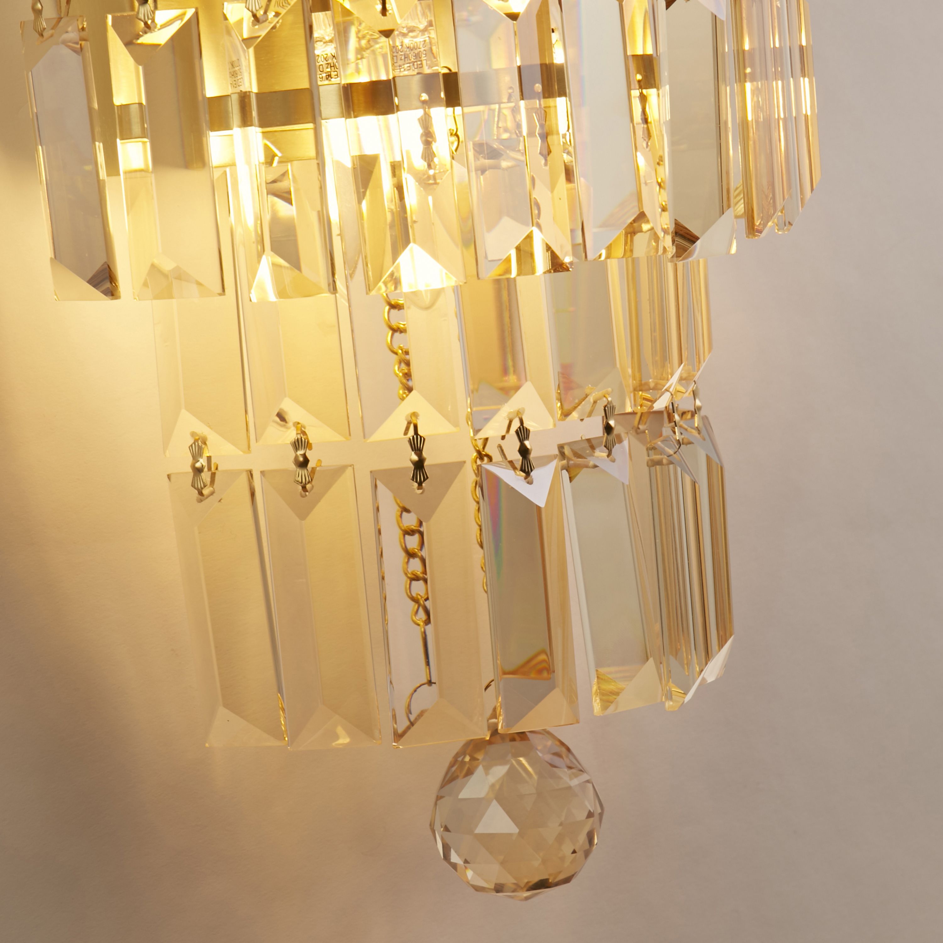 Close up of the Empire wall light's champagne crystal prisms and satin brass frame, showing the faceted glass detail lit from within