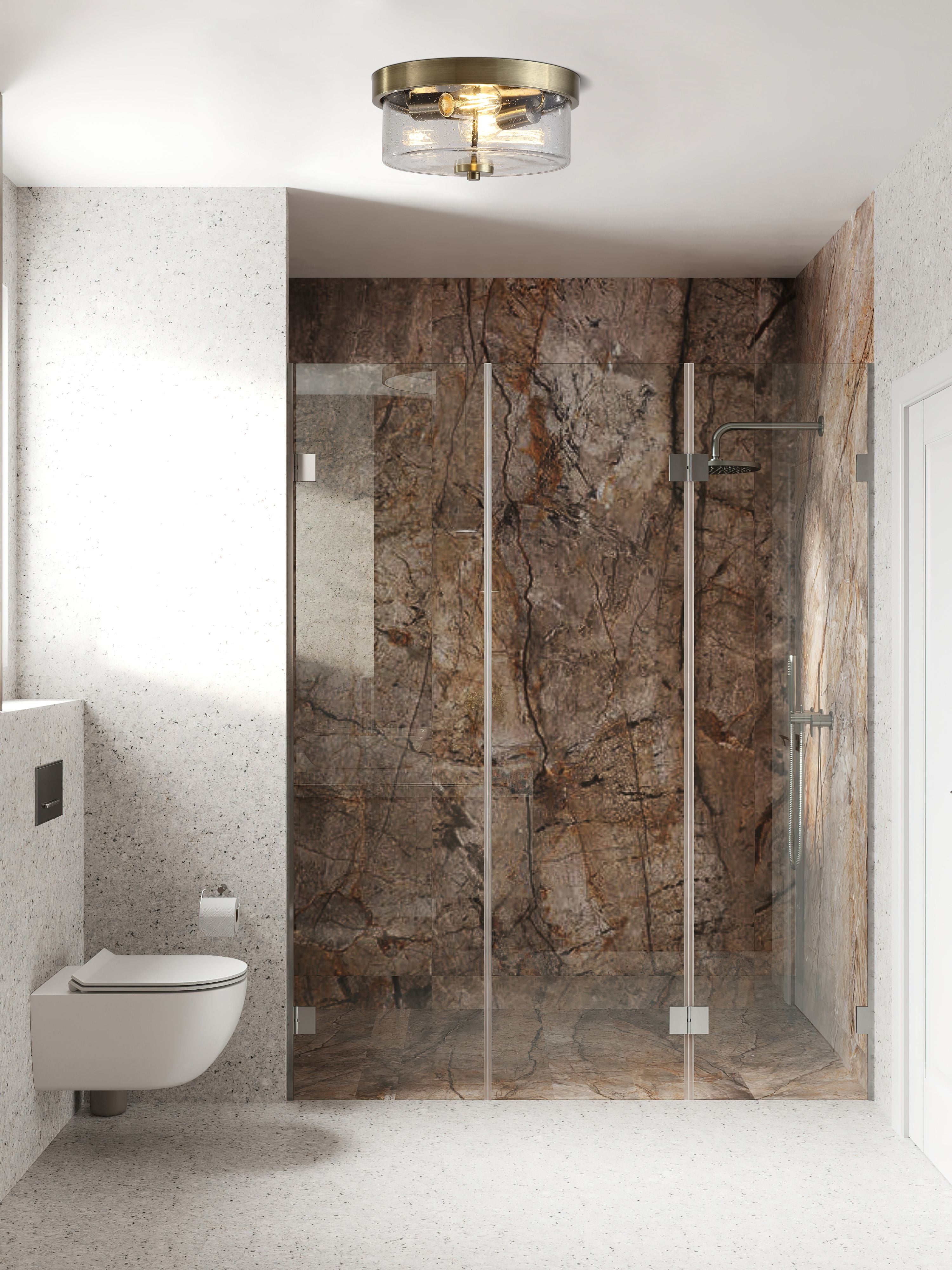 A seeded glass drum ceiling light in an antique brass finish, shown fitted above a walk in shower with marble tiled walls