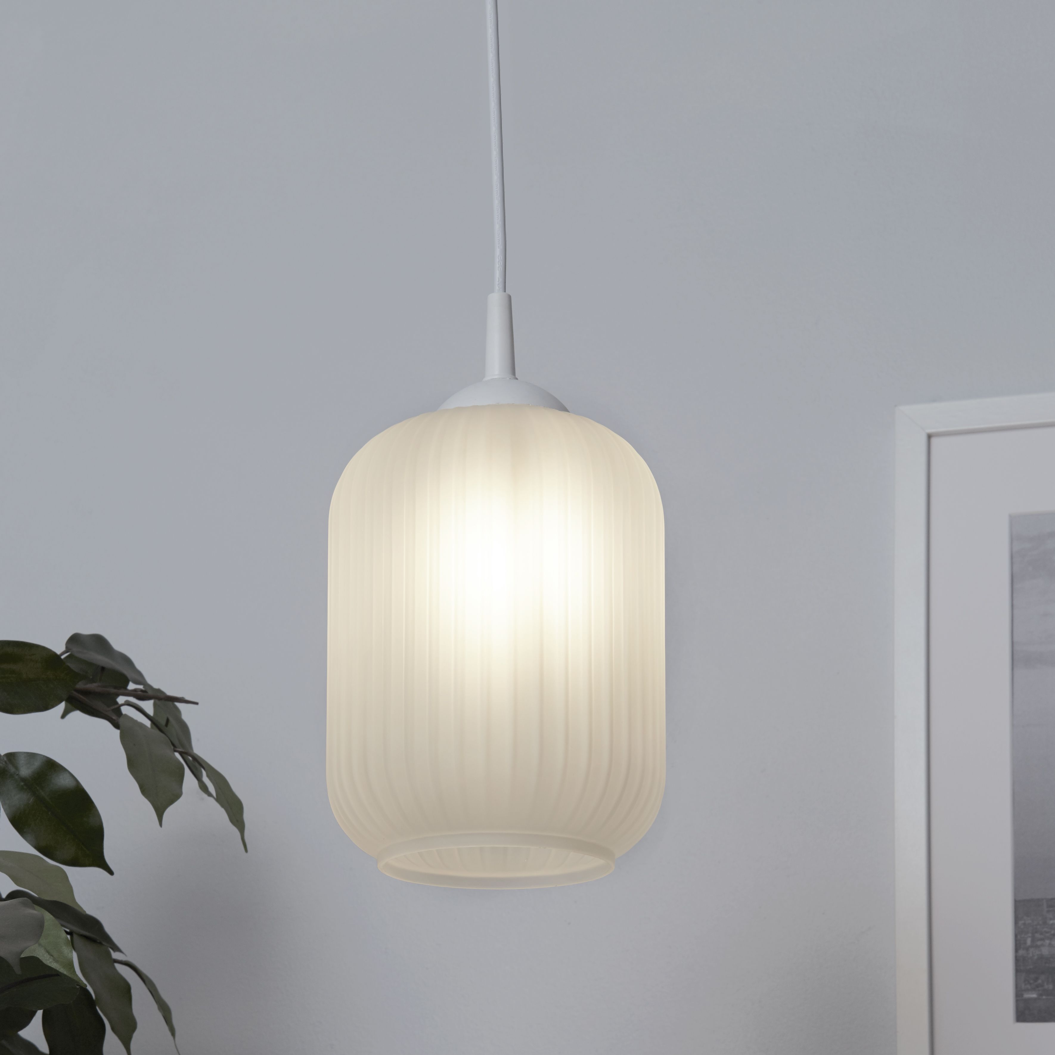 Searchlight Pearl pendant light lit and hanging in a styled white room with a house plant and framed picture