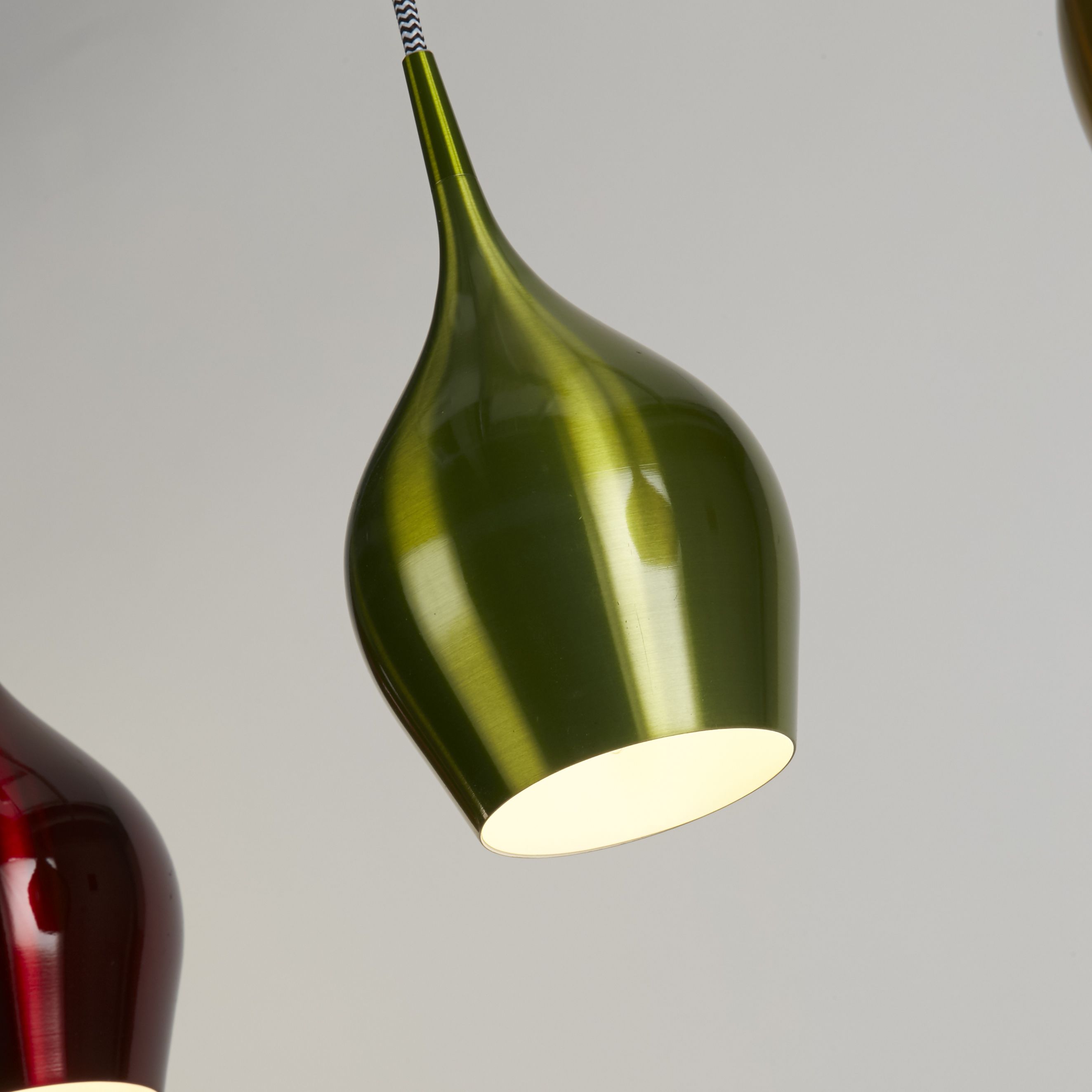 Close up of the green gloss teardrop shade on the Vibrant pendant, showing the metallic finish and white interior reflector, with the red shade visible alongside