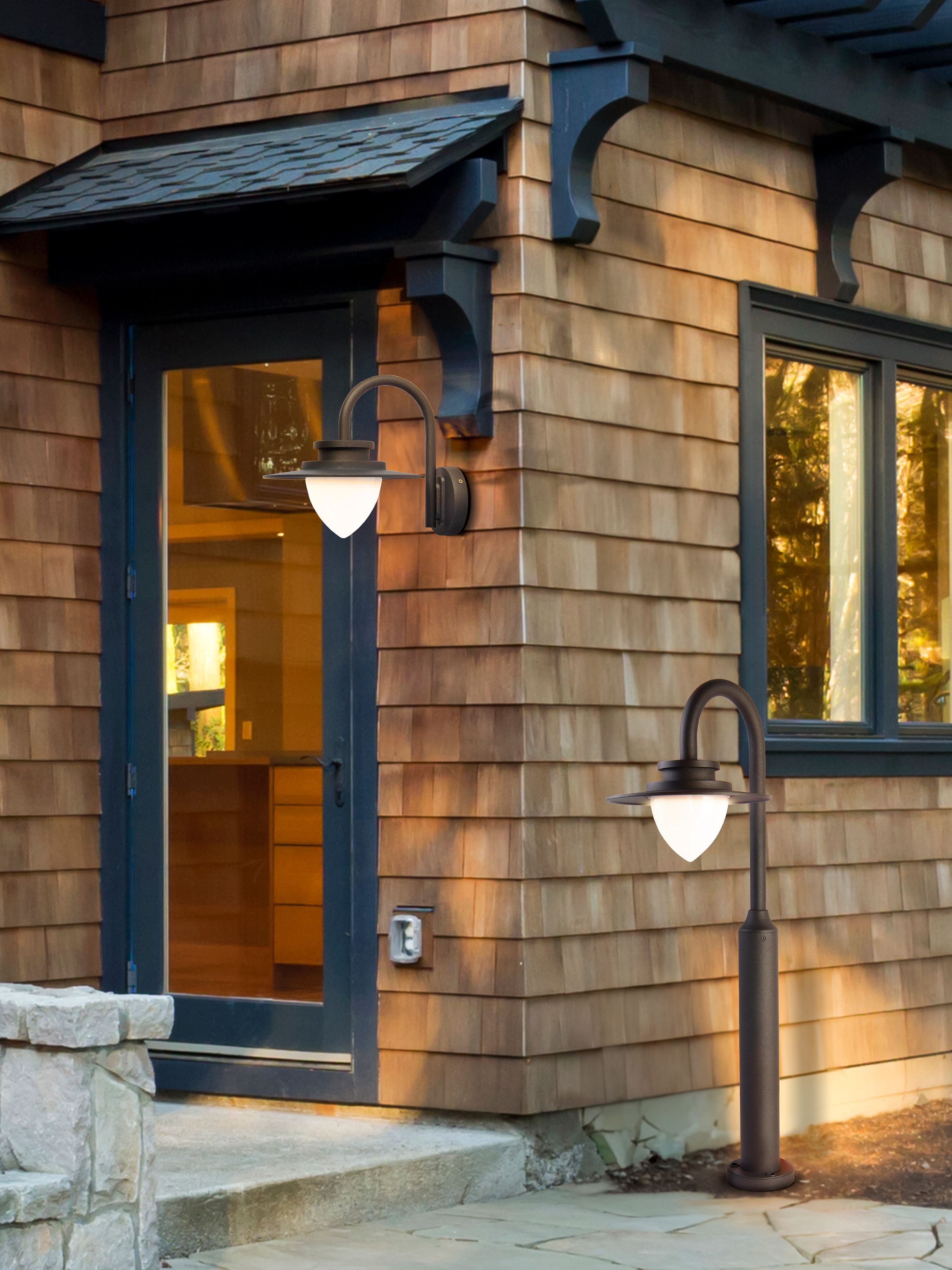 Texas outdoor bollard light lit at night beside a garden path, with a matching wall light lit on the shingled house behind it
