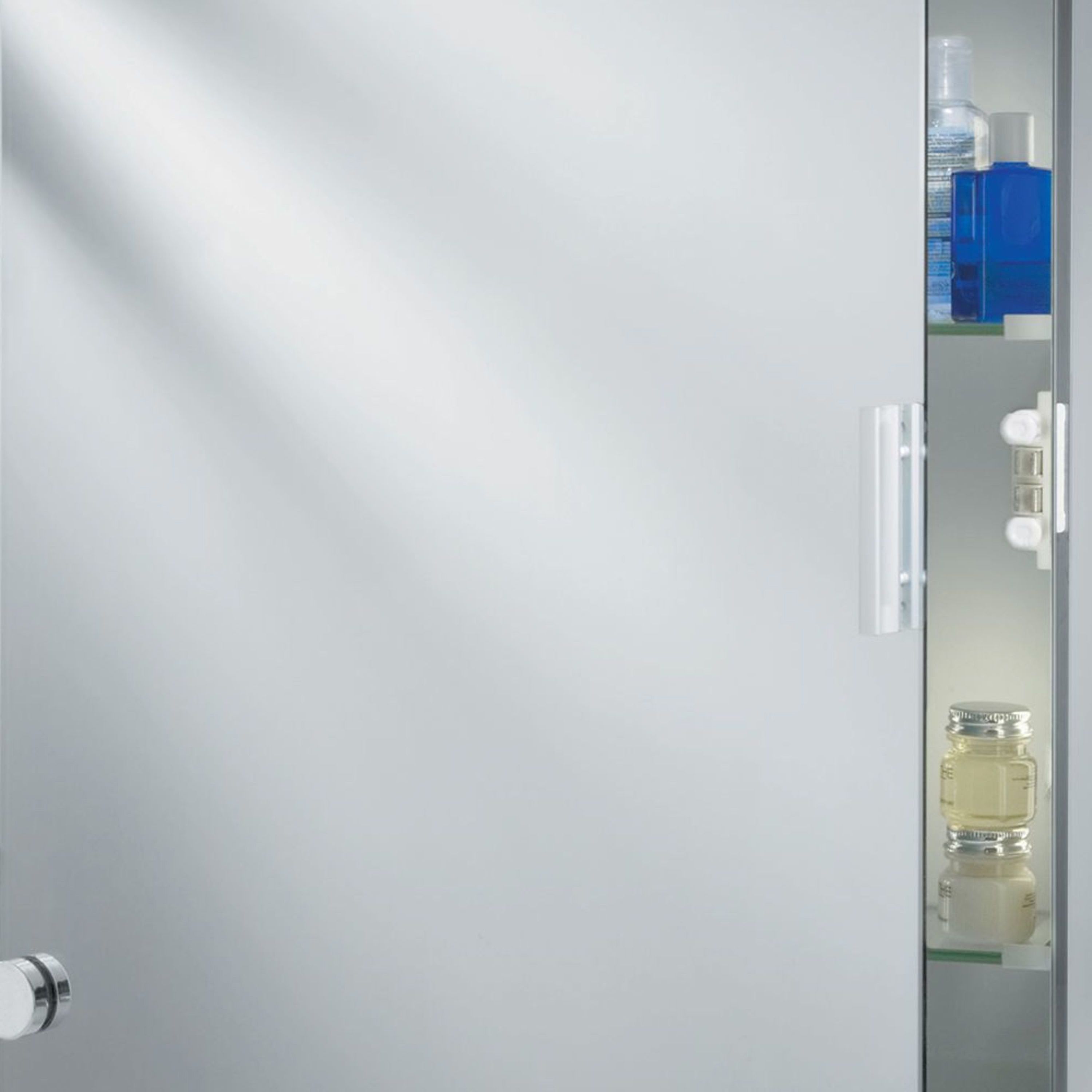 Close up of the mirror cabinet's shelved interior, showing toiletries, the door hinge and handle, and the mirrored back panel