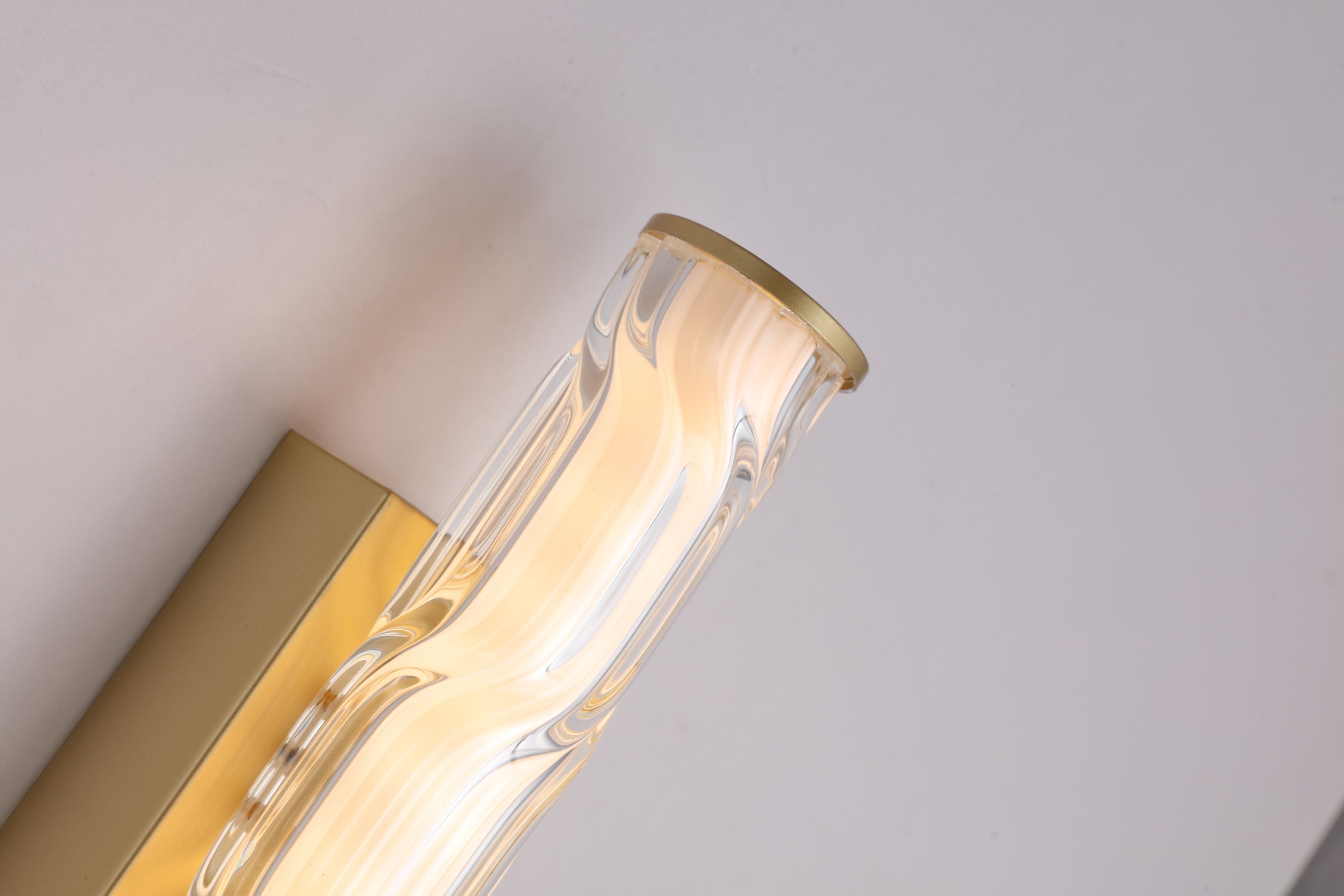 Close up of the Vibrate wall light's top end cap in matt gold, showing the wave ridged glass texture