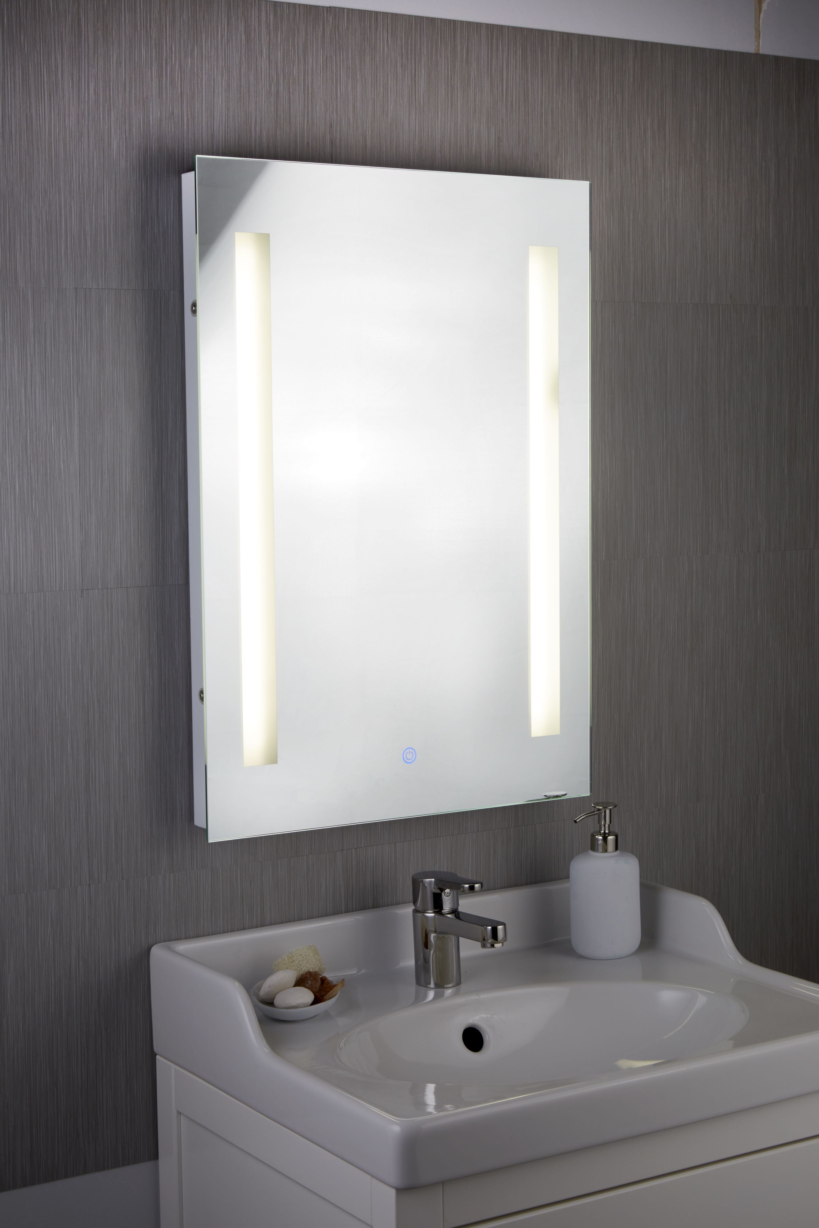 Searchlight chrome bathroom mirror styled above a small pedestal sink, both light strips lit, in a dark tiled bathroom