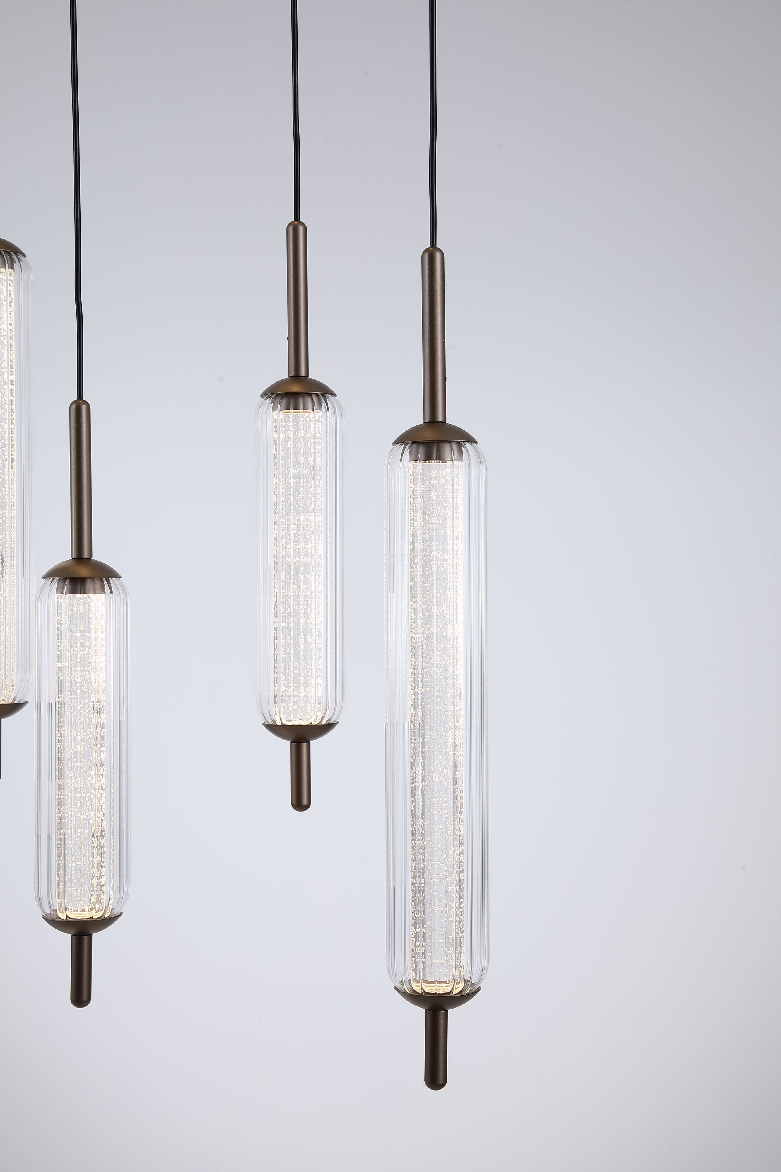 Close up of three Searchlight Cattail pendant glass tube drops, showing the ribbed clear glass and latte metal end caps lit from within