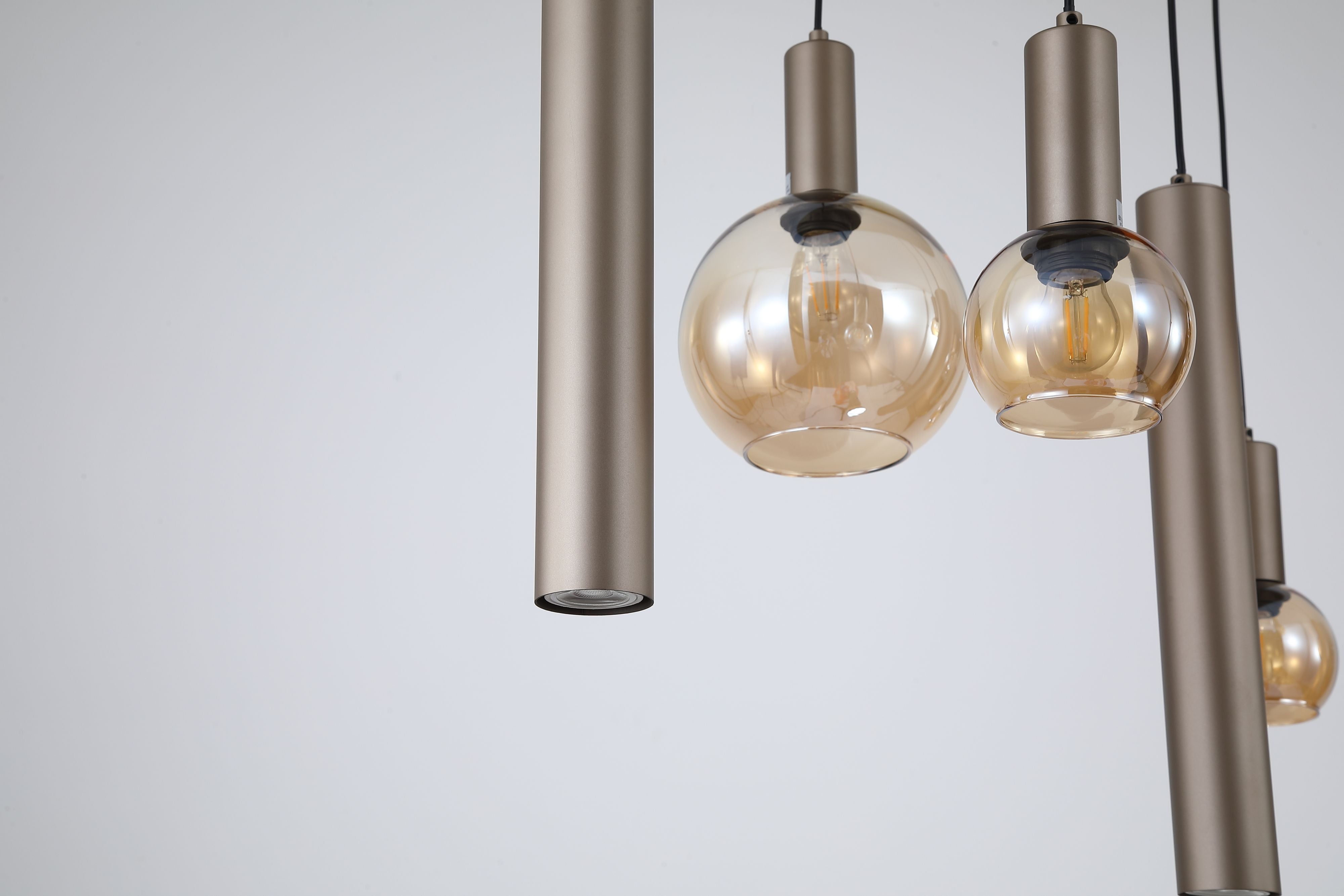 Close up of the Lyon pendant's amber glass globe shades and latte metal cylinder drops with the filament bulbs glowing inside