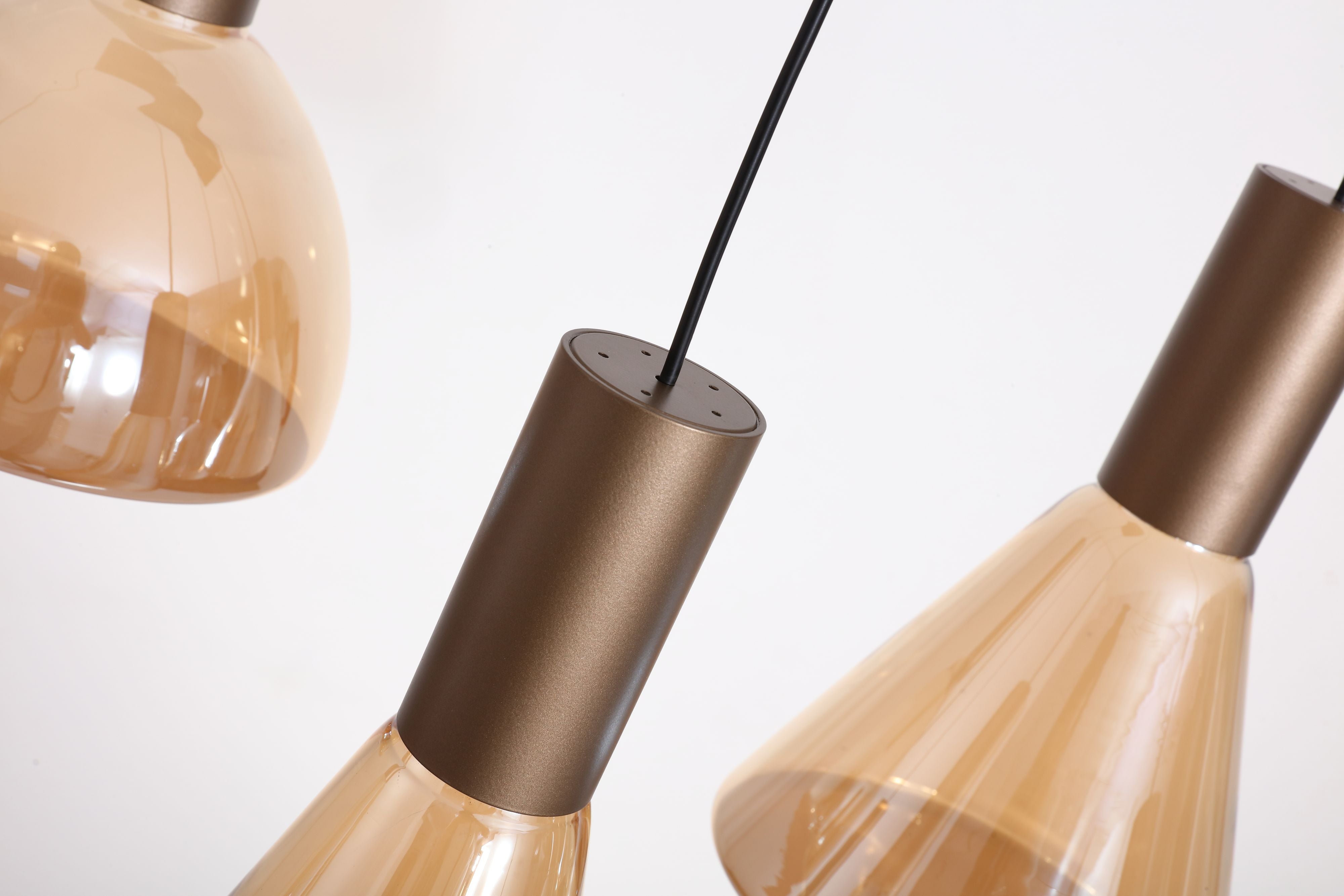 Close up of the latte bronze shade cap and suspension cable on the Searchlight Cannes 6 Light Pendant, with cone and dome amber glass shades either side
