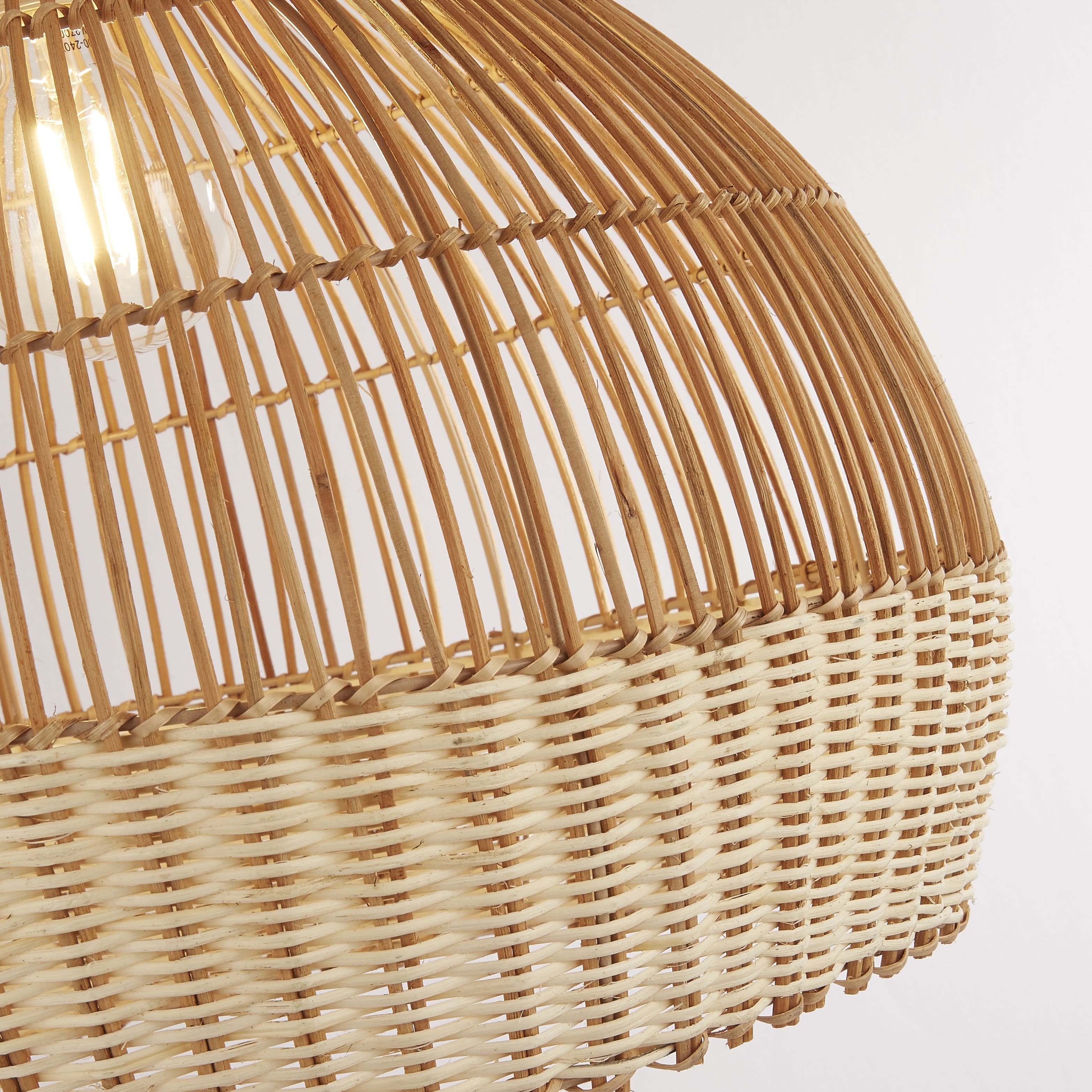 Close up of the Bali pendant shade showing the open cane weave strands and the paler, tightly woven base band, with the bulb lit inside