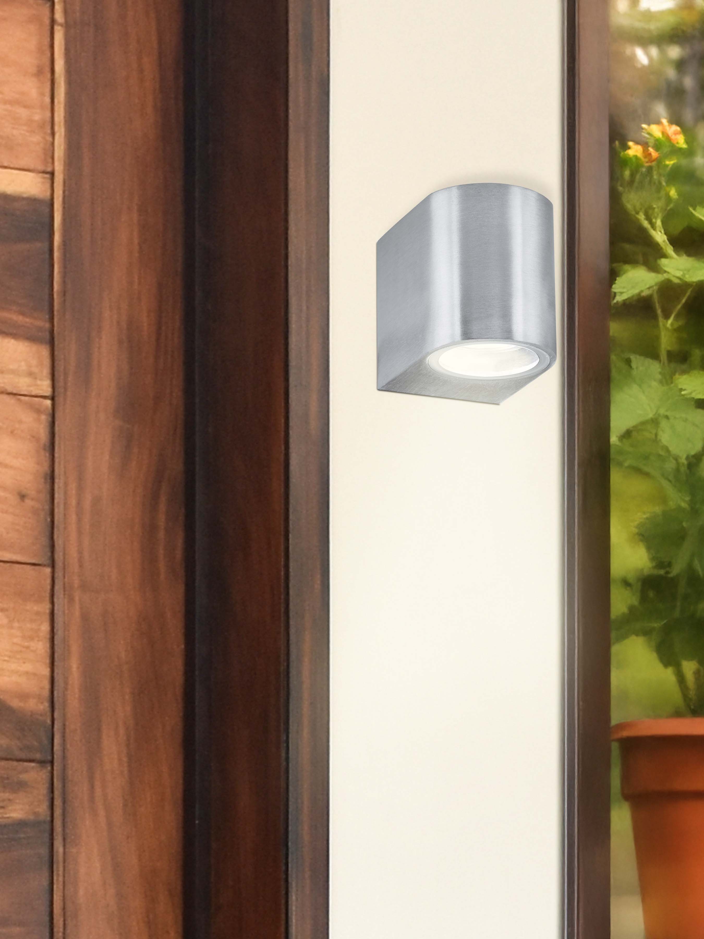Eiffel satin silver outdoor wall light mounted beside a wooden front door, lit next to a potted plant