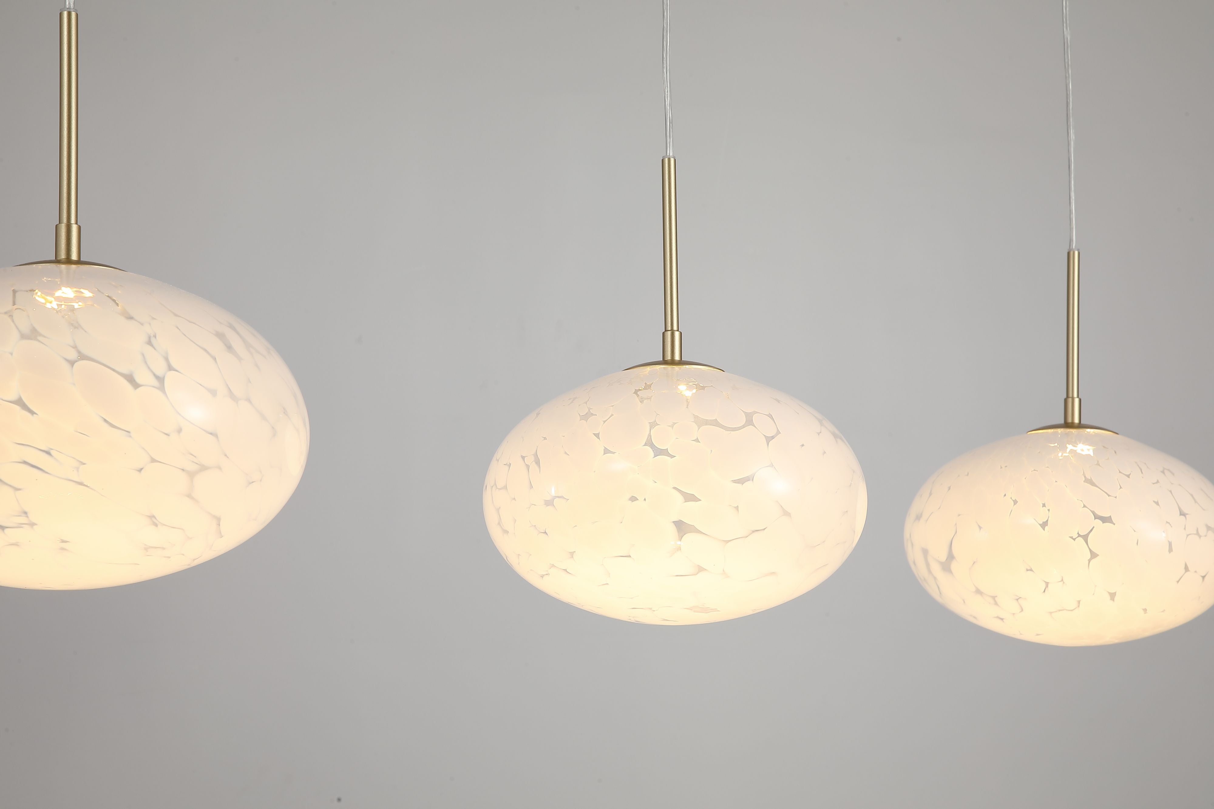 Close up of three lit Searchlight Confetti LED Bar Pendant shades showing the mottled confetti glass and gold rods