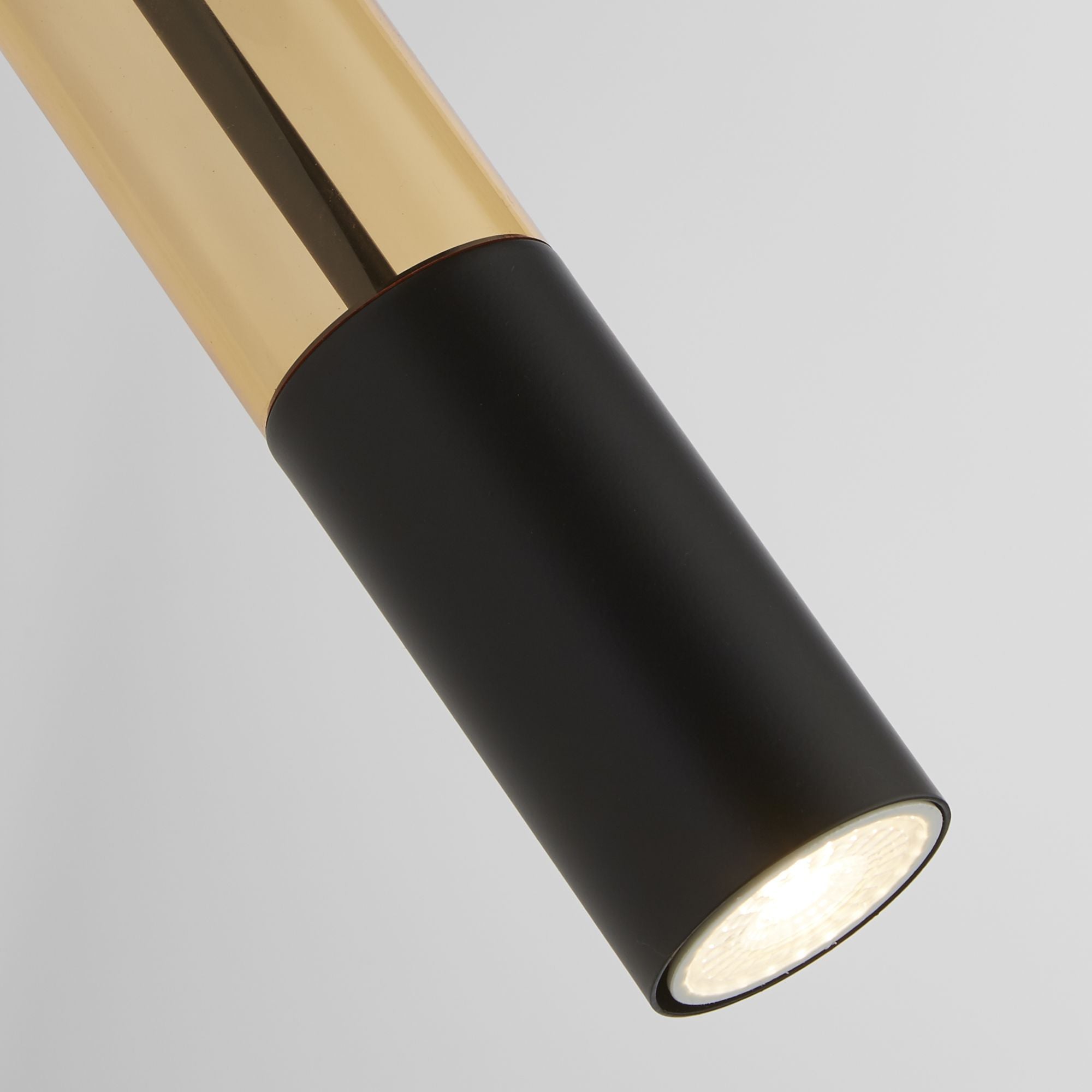 Close up of the Searchlight Merrygold wall light head, showing the amber acrylic tube, matt black cylinder and lit GU10 spotlight
