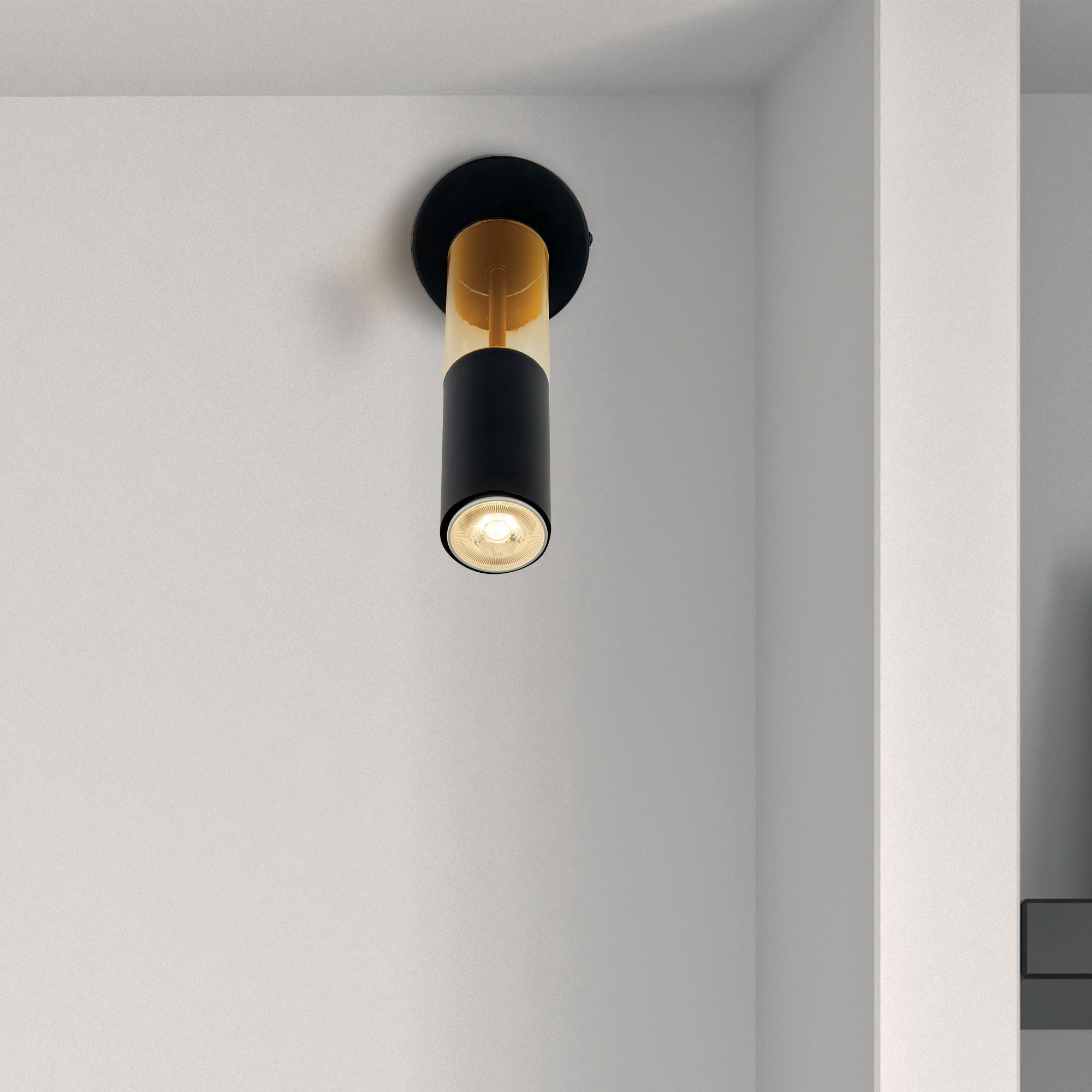 Searchlight Merrygold wall light mounted in a hallway, black fitting with amber acrylic accent lit against a light grey wall