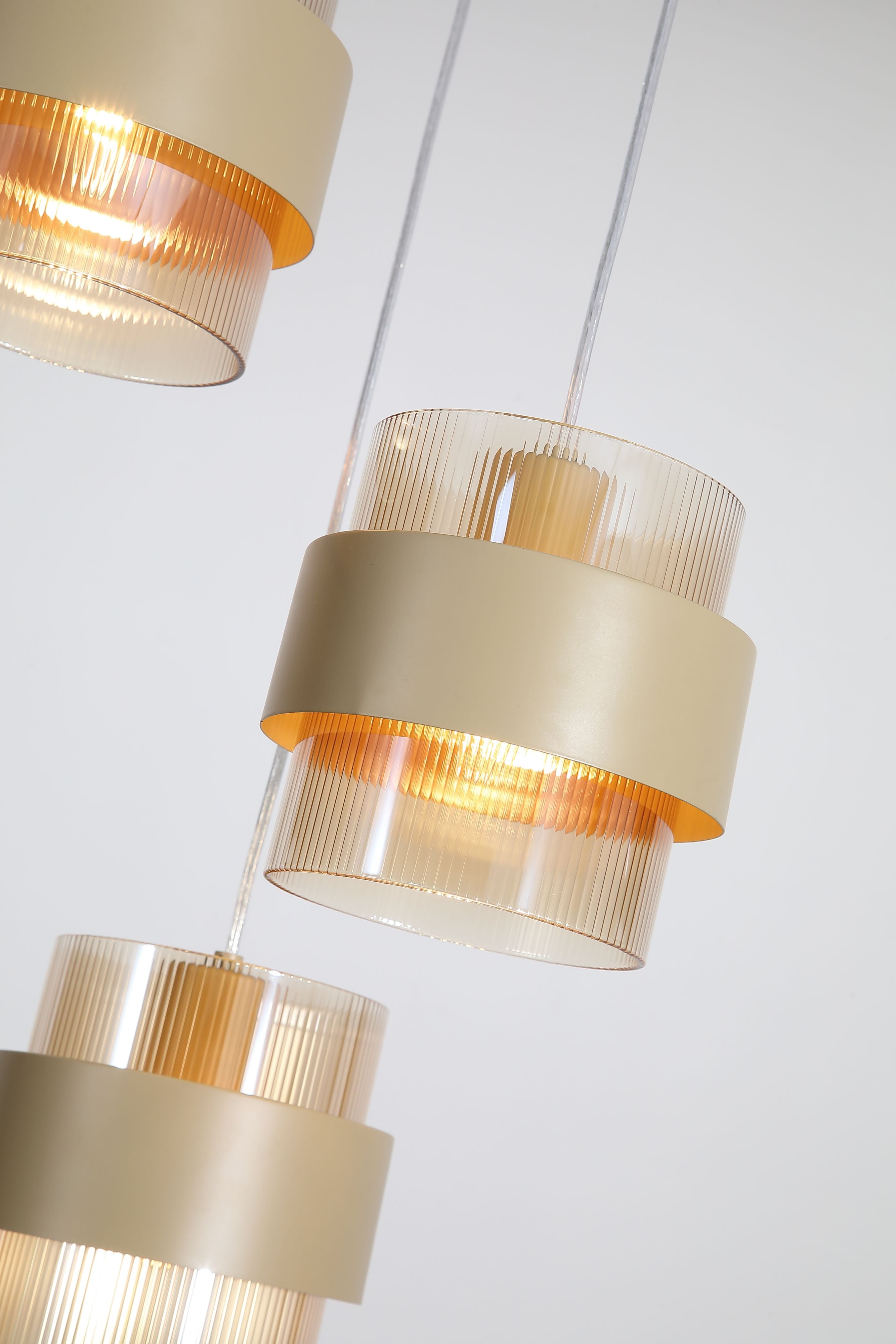 Close up of two Searchlight Royal multi drop shades showing the ribbed amber glass and sand metal band lit from within
