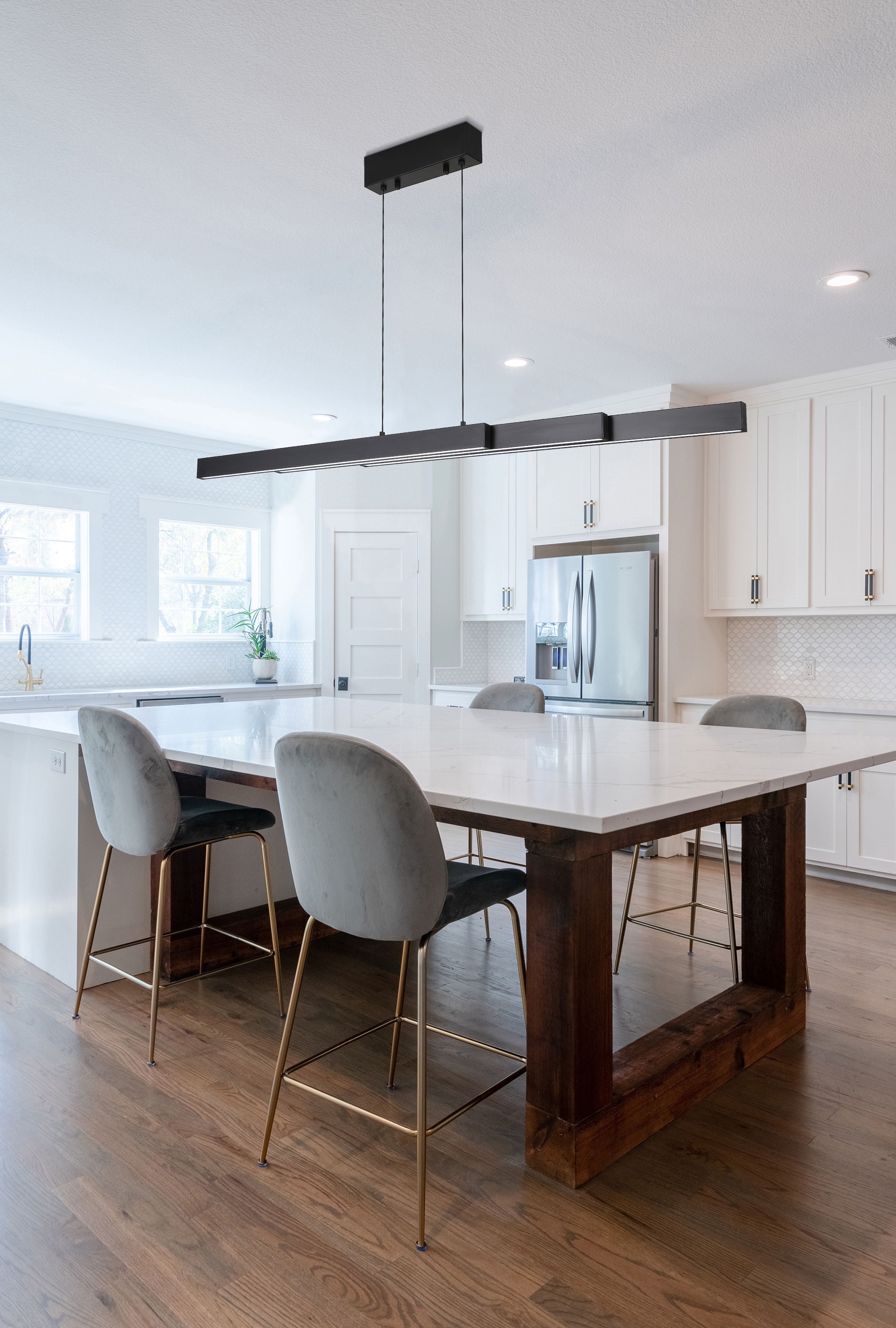 Searchlight Linear LED pendant in matt black styled above a kitchen island dining table with grey velvet chairs and a stainless steel fridge
