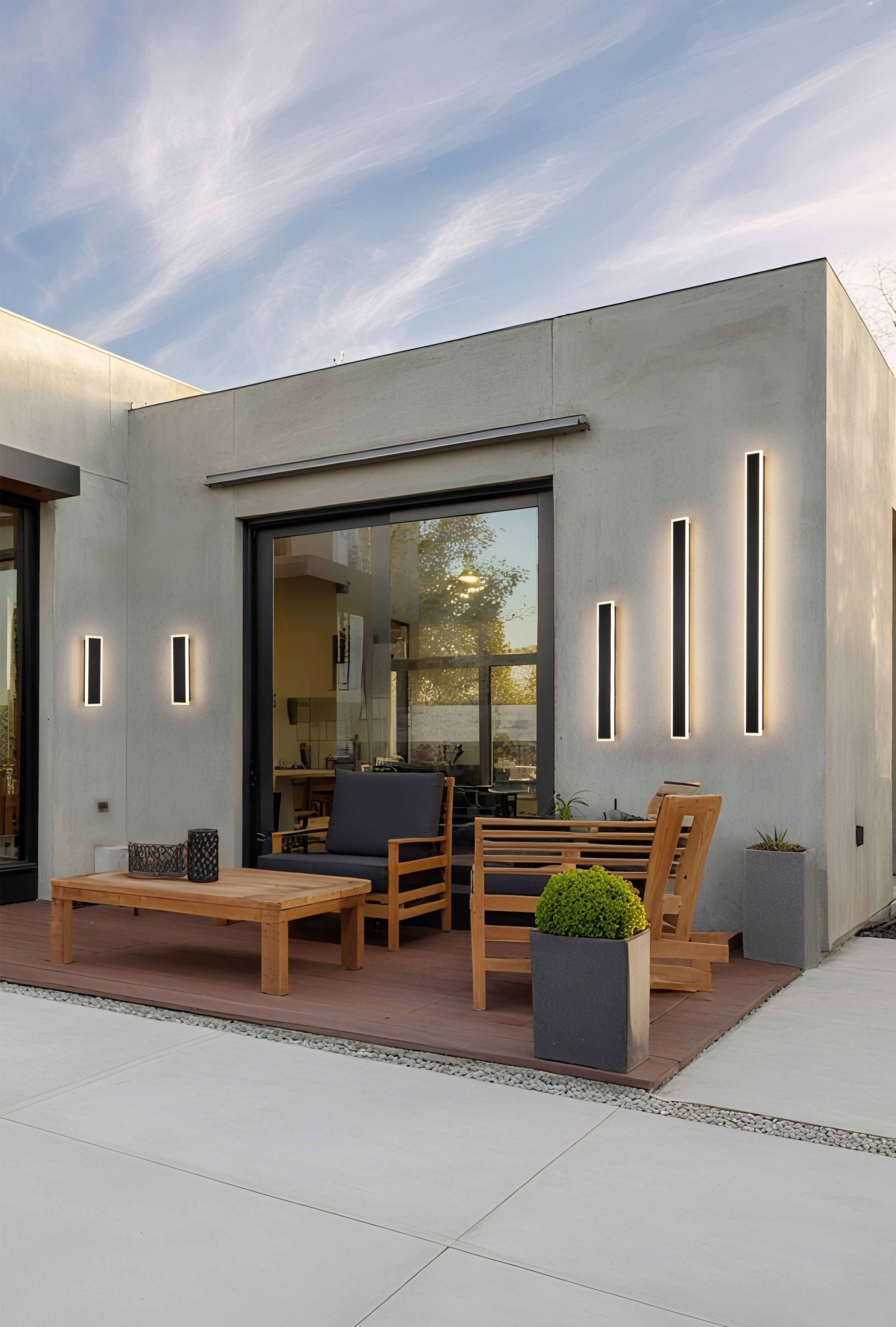 Bordo II Square wall lights installed in pairs on a modern concrete patio wall at dusk, lit, next to wooden outdoor seating and potted plants