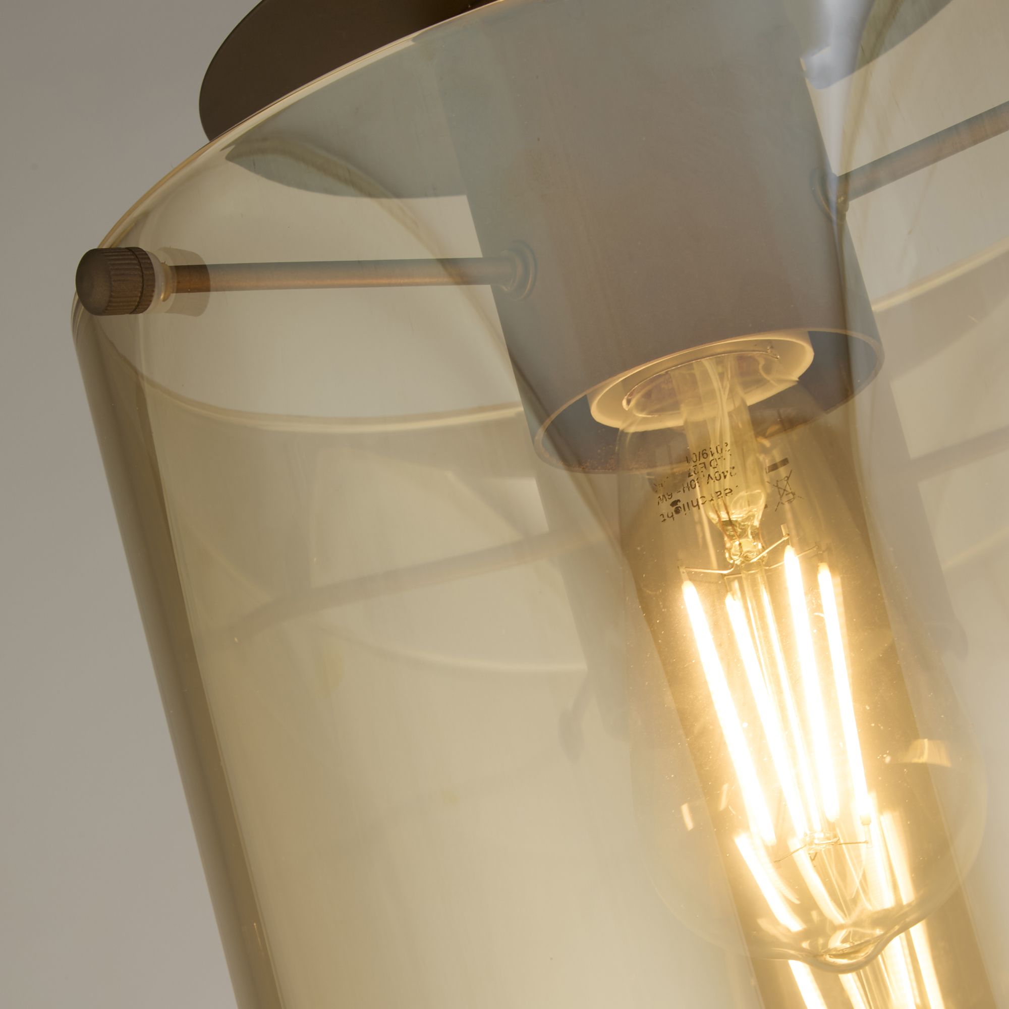 Close up of the mocha metal fixing pin and amber glass shade on the Searchlight Sweden 1 Light Flush, with the filament bulb and its markings visible
