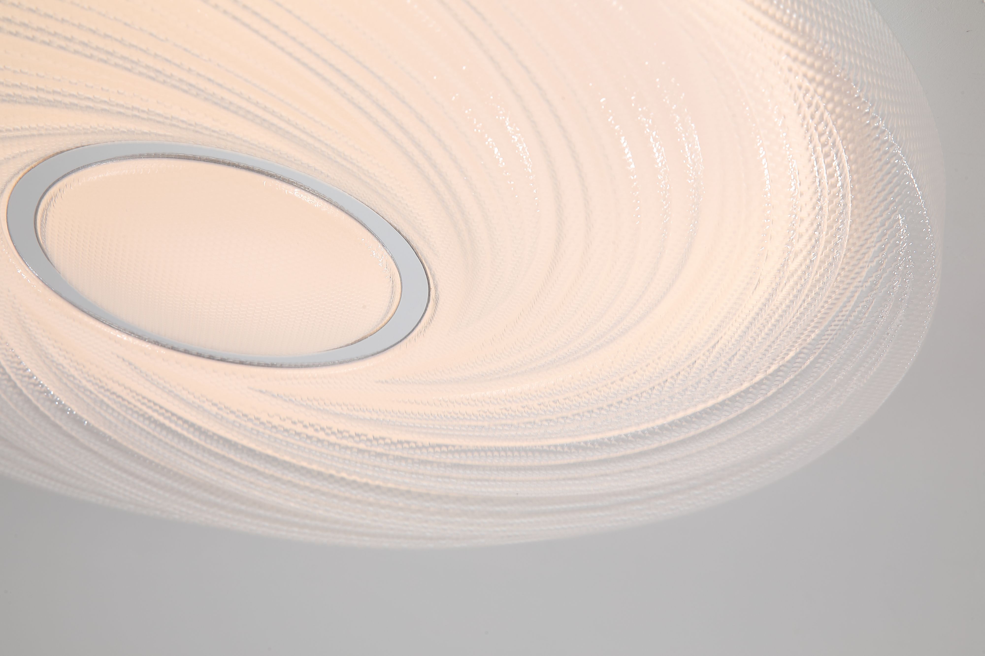 Close up of the Aura flush ceiling light fitted to a ceiling, showing the spiral textured acrylic diffuser and chrome centre ring