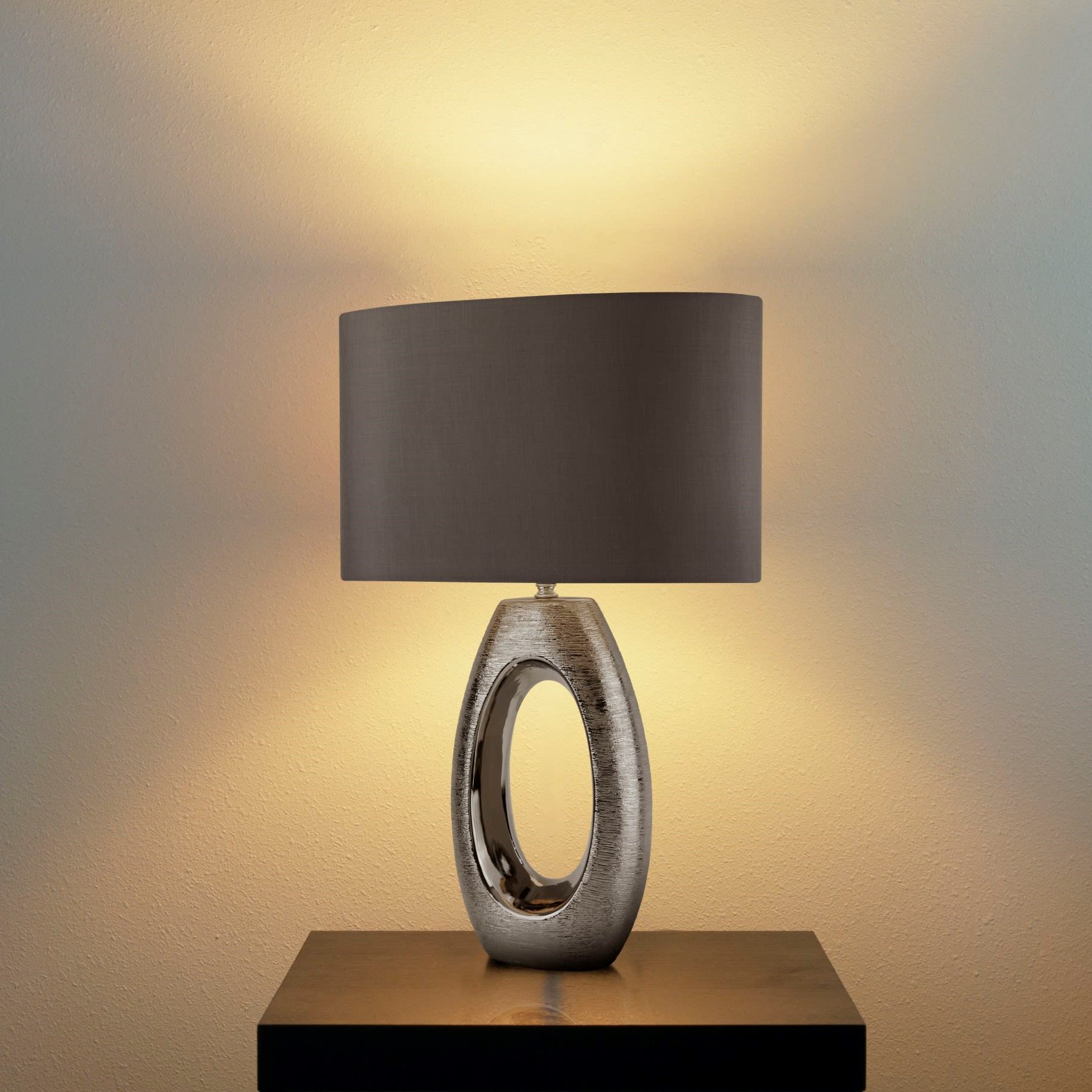 Artisan table lamp switched on and glowing, styled on a shelf against a plain wall