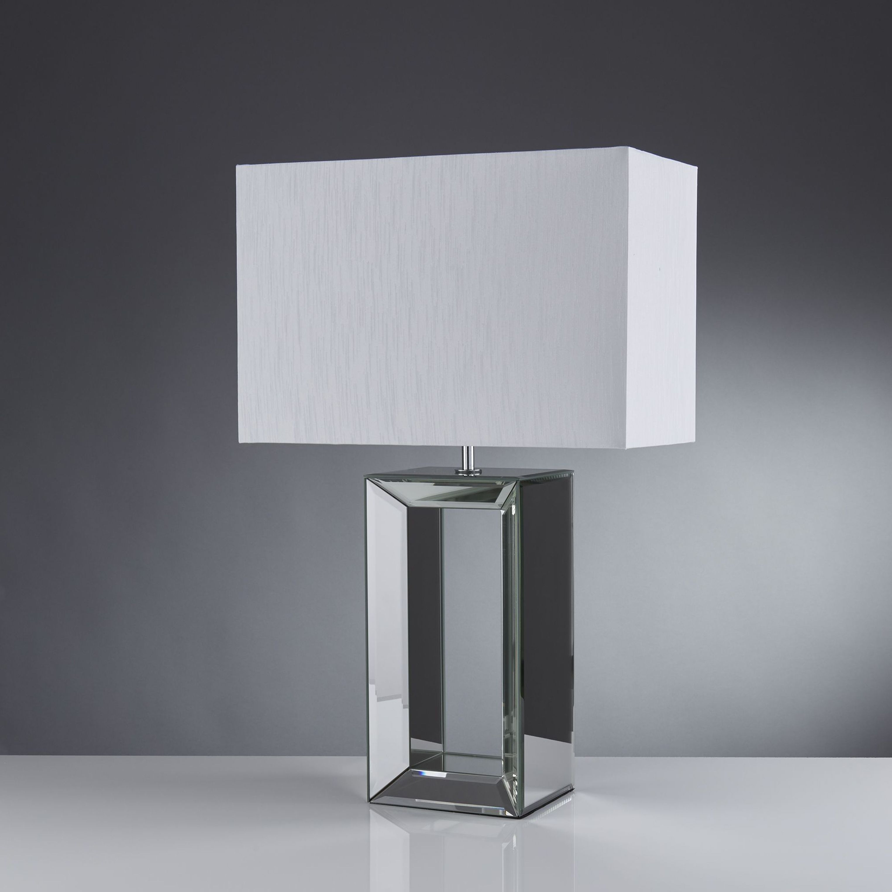 Searchlight mirror table lamp with hollow mirrored glass base and rectangular white faux silk shade, styled shot on a dark gradient background