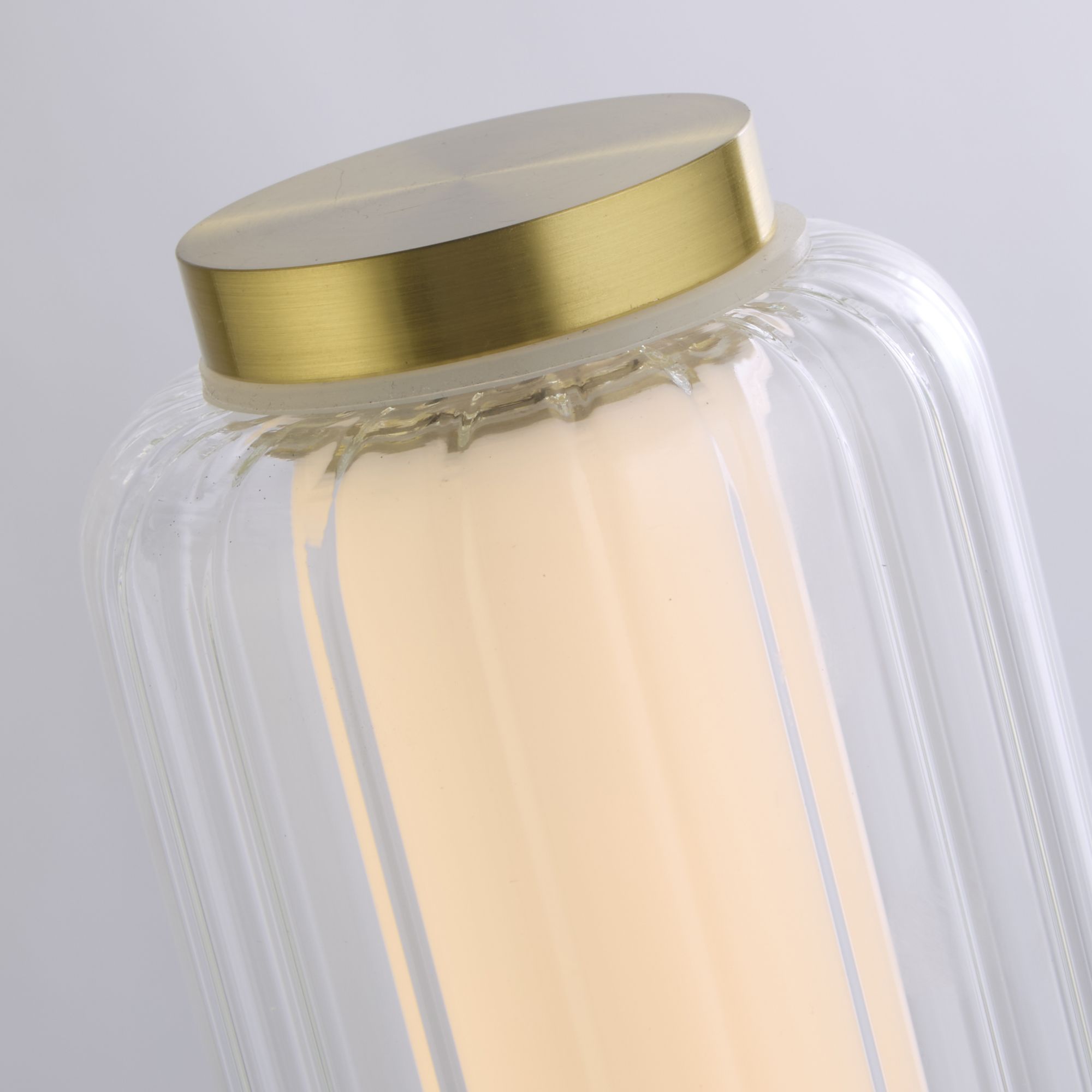 Close up of the Searchlight Mod LED Table Lamp showing the satin brass cap and ribbed glass column lit from within