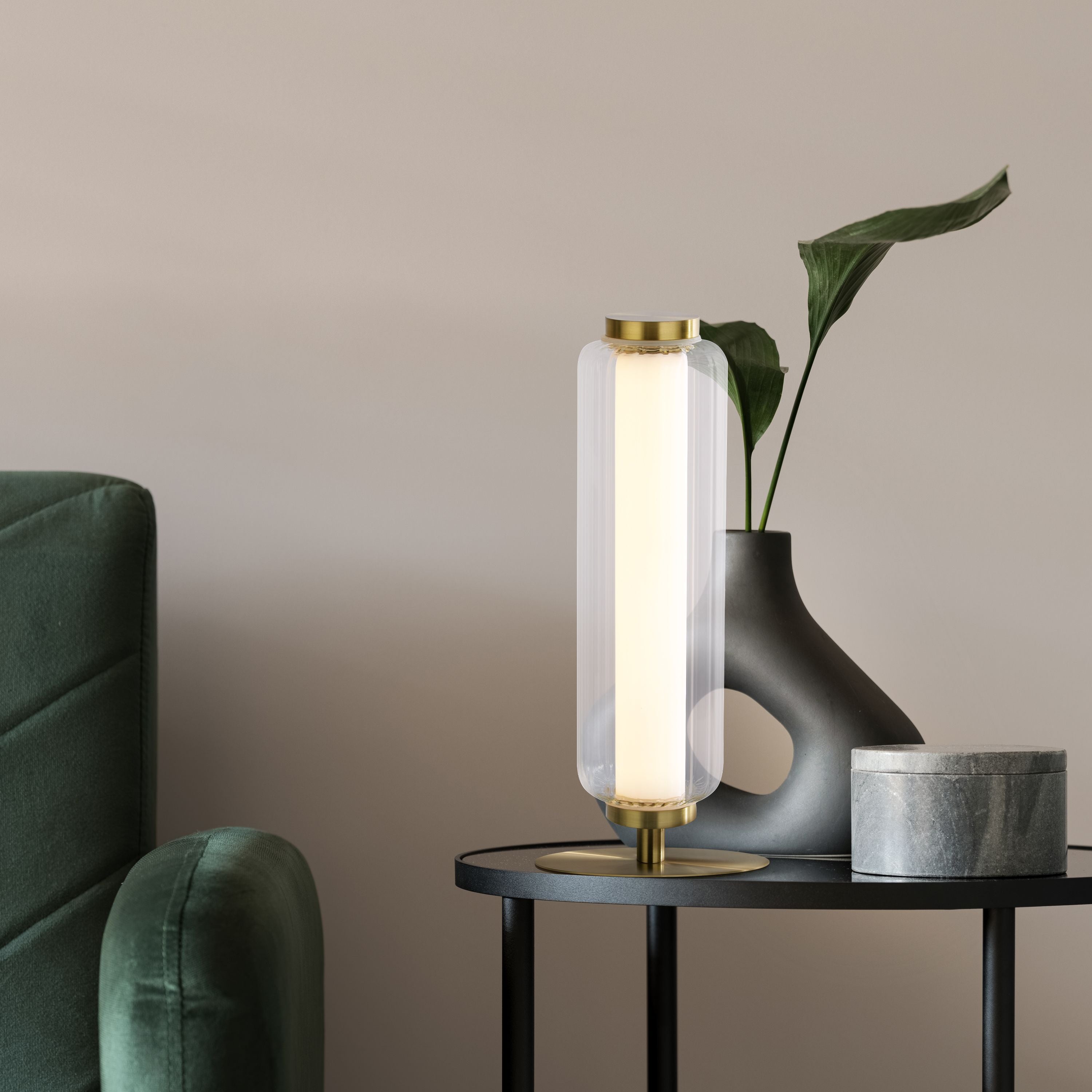 Searchlight Mod LED Table Lamp styled on a side table beside a dark vase and green plant, shown lit in a living room