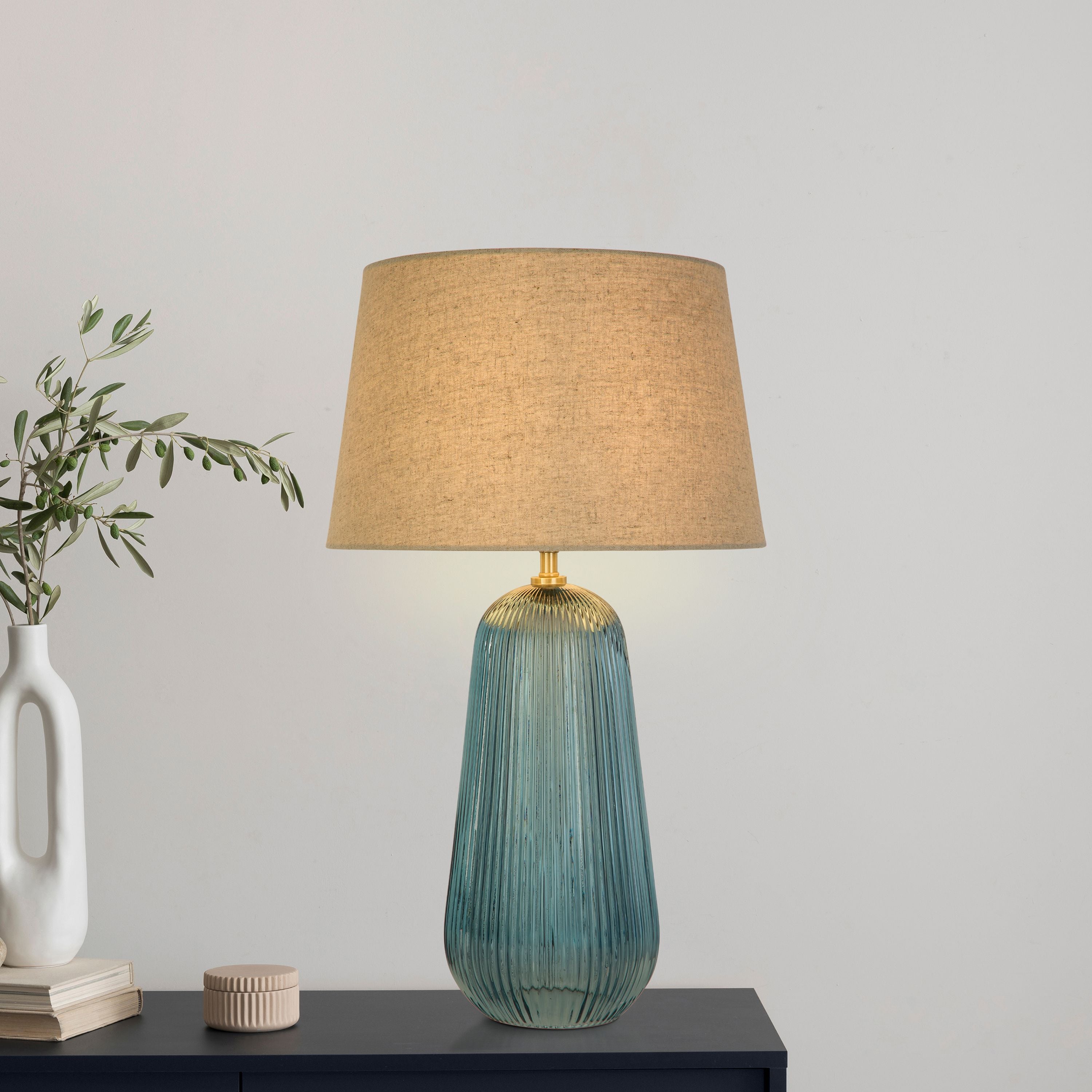 Cameo blue glass table lamp styled on a dark console table next to an olive branch and books