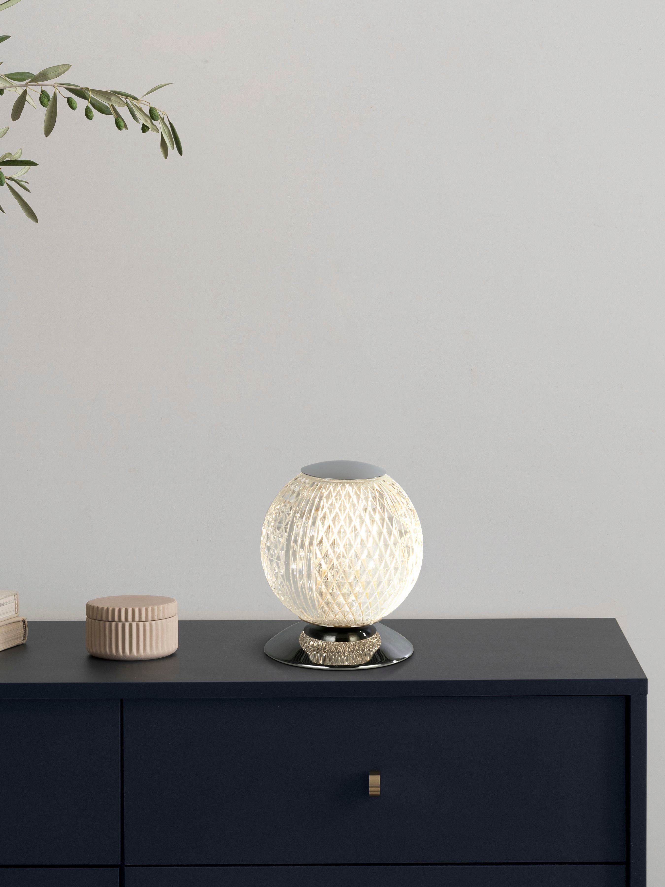 Searchlight Allure table lamp in chrome styled on a dark blue console table beside a ceramic trinket pot and an olive branch