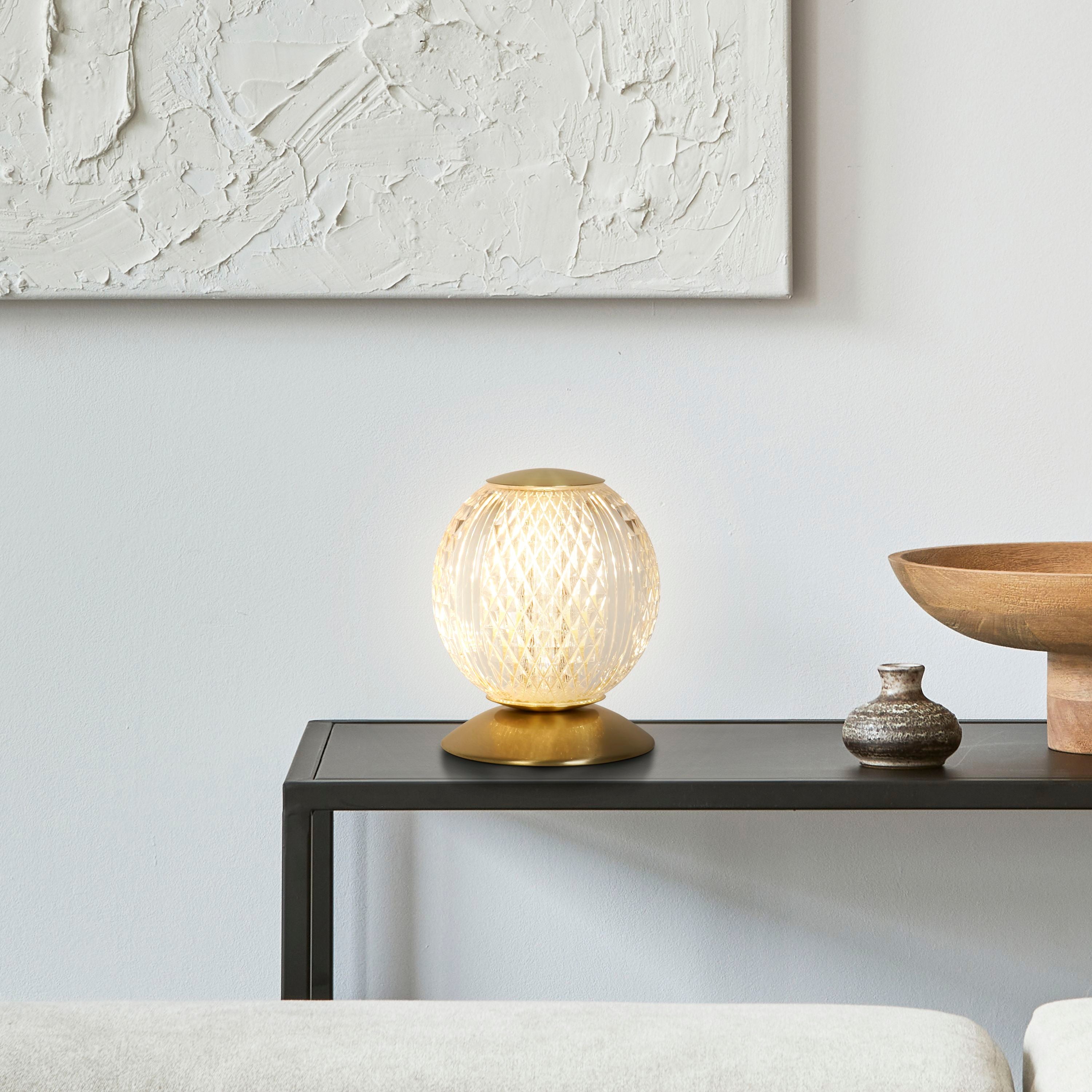 Allure table lamp in satin brass styled on a console table beside a ceramic vase and wooden bowl