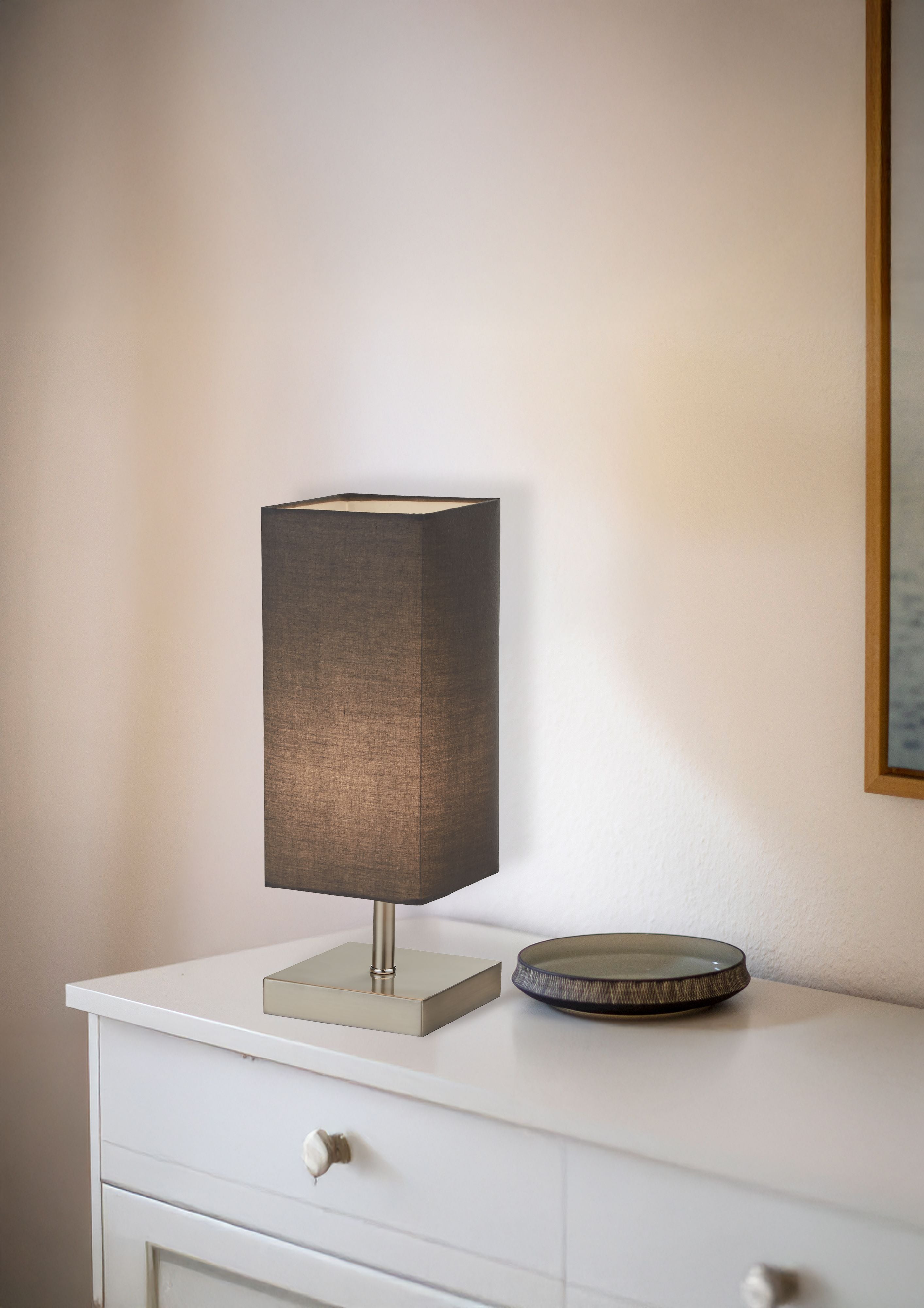 Valley table lamp lit on a white bedroom dresser, styled next to a small trinket dish
