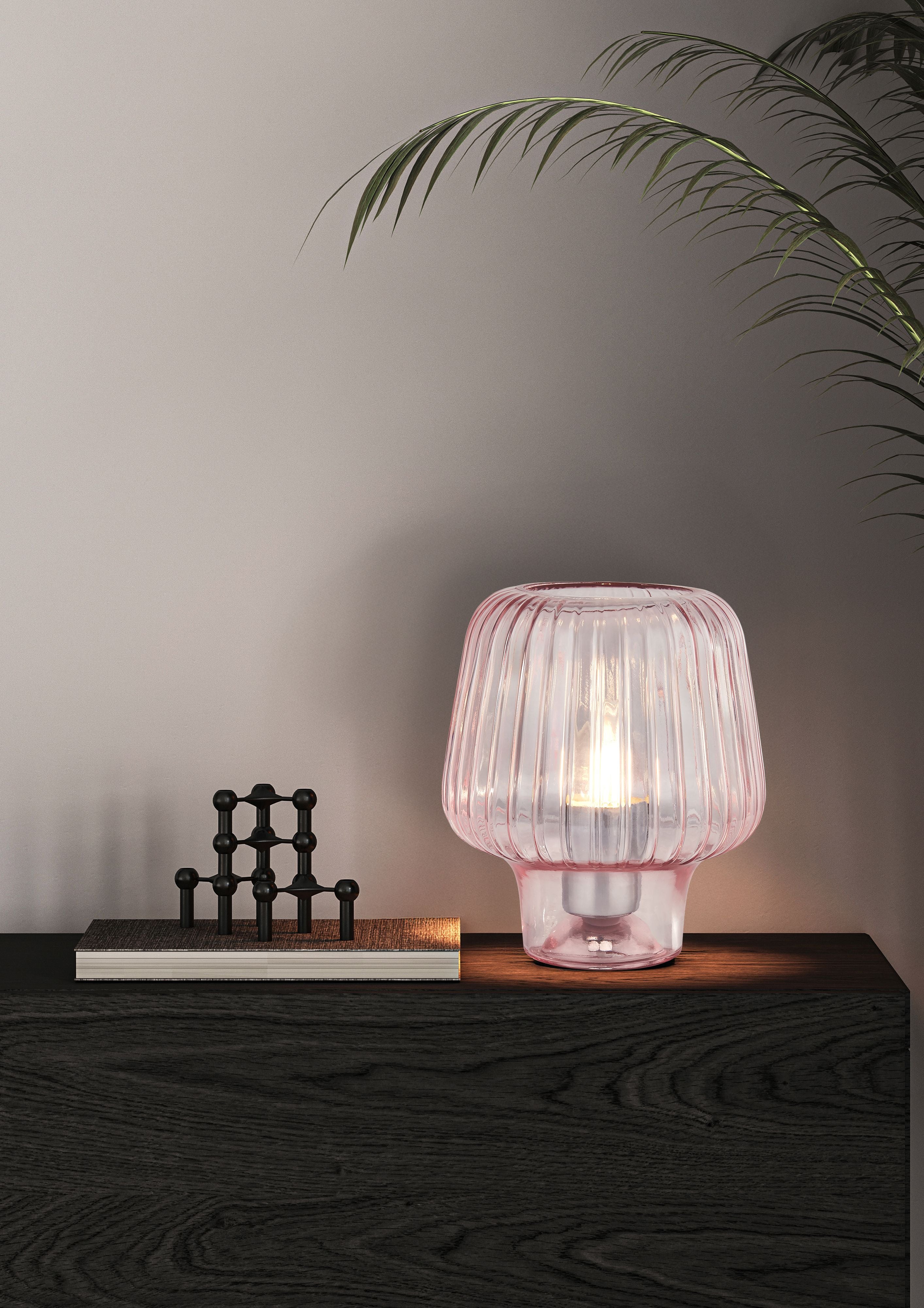 Searchlight Aria table lamp in pink ripple glass, lit, styled on a dark wood console table beside a book and a small ornament