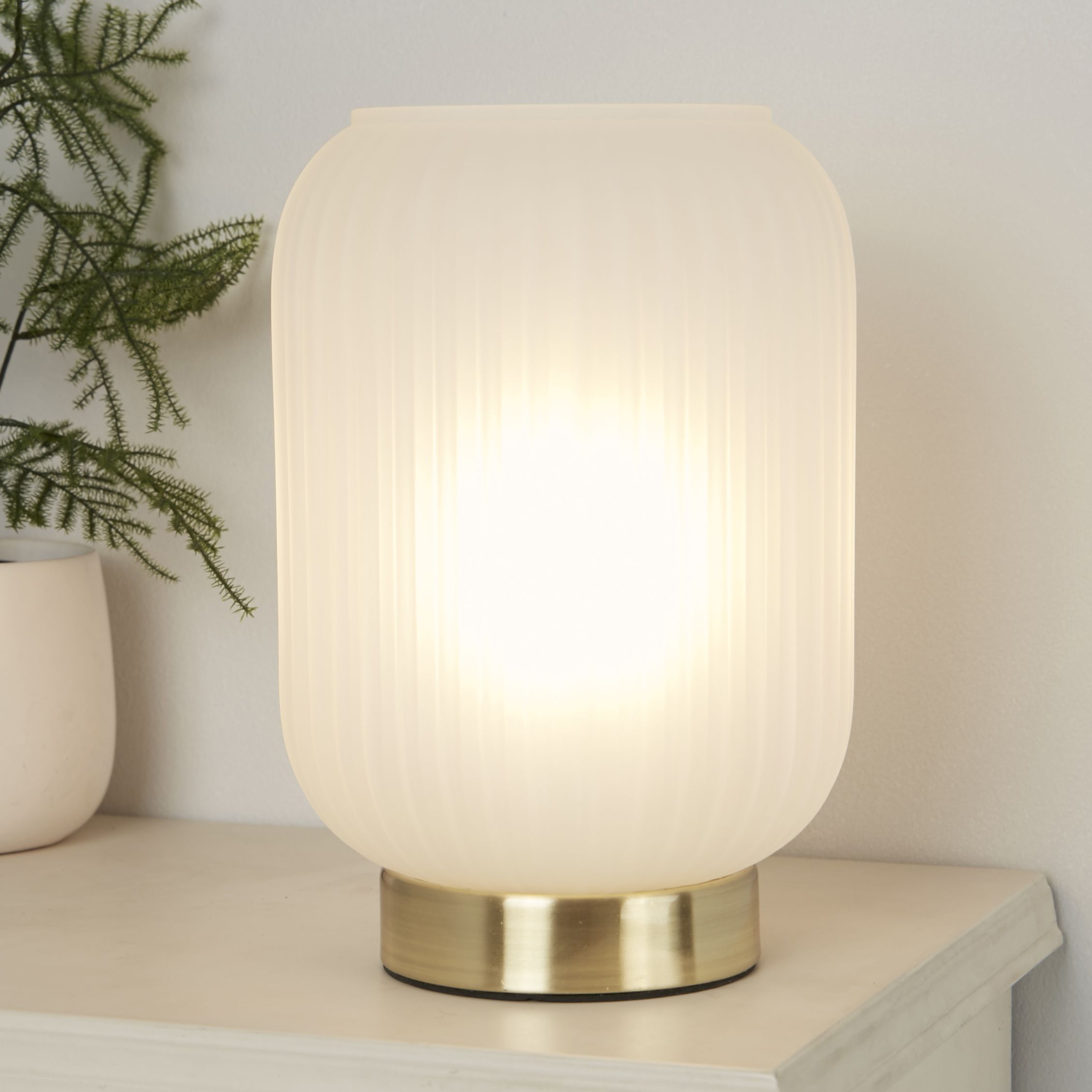 Searchlight Pearl table lamp lit on a bedside shelf, styled with a small plant in the background