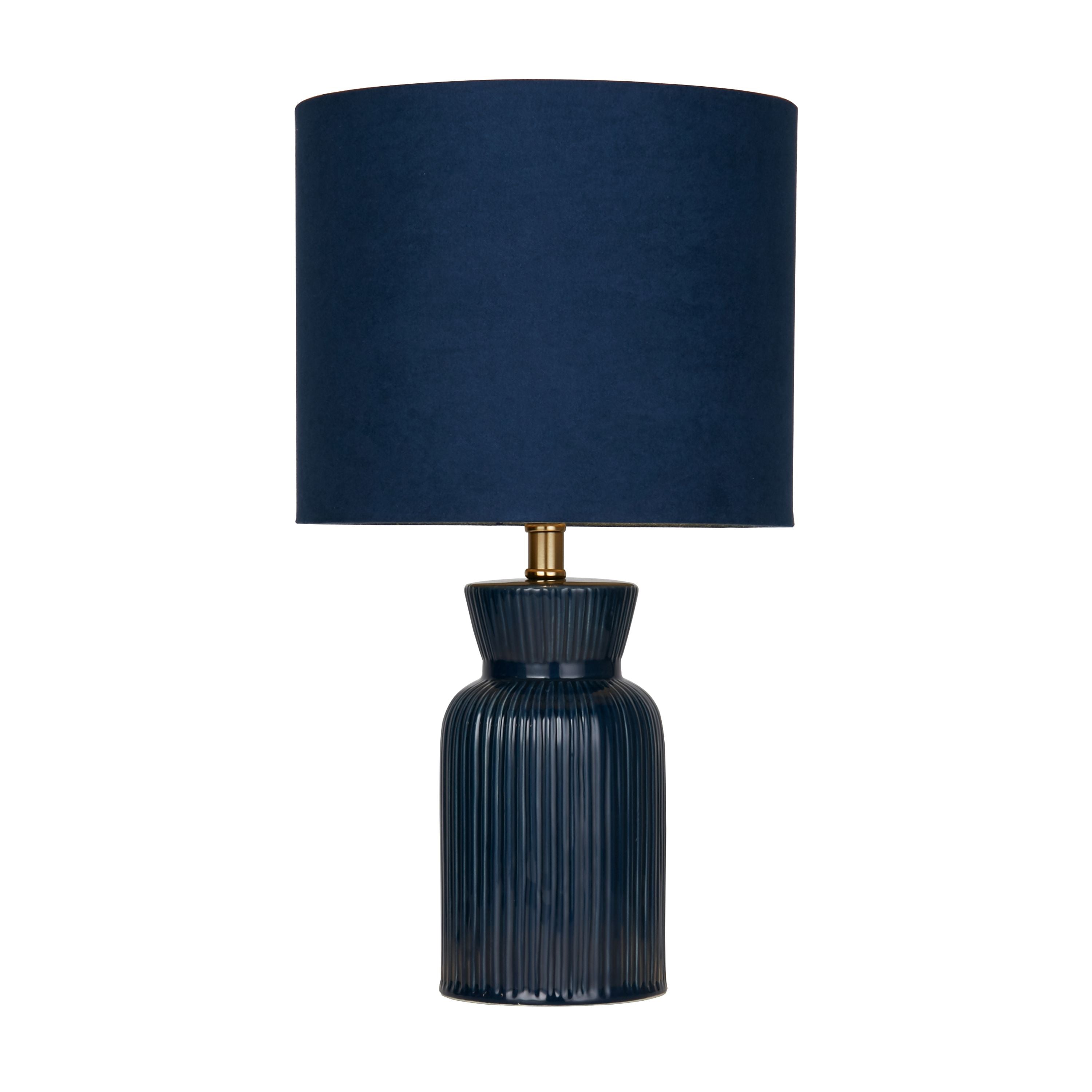 Navy ceramic table lamp with a ribbed body, fluted neck and brass fitting, topped with a matching navy fabric drum shade, studio shot