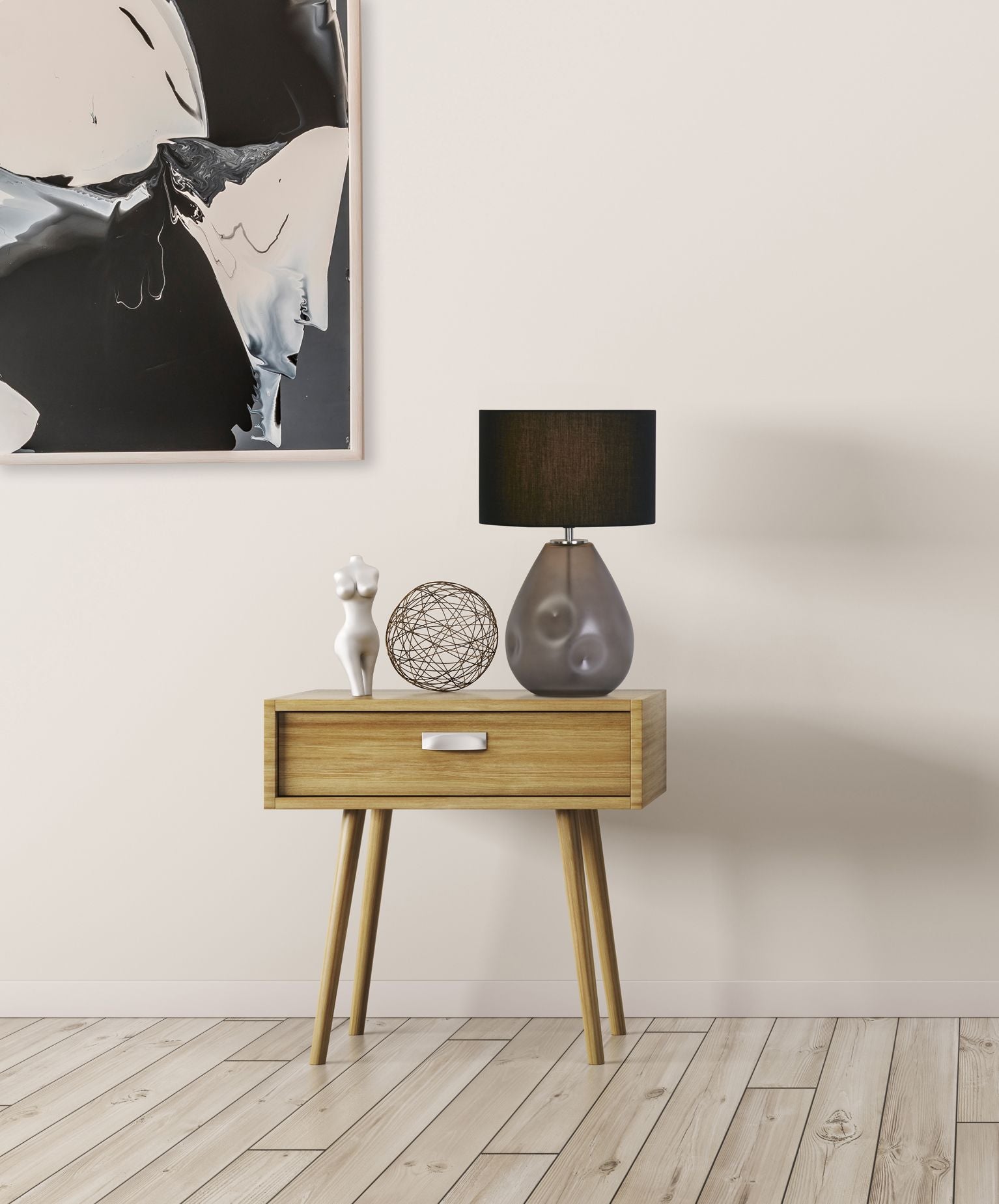 Searchlight Devon table lamp in black lit on a wooden nightstand, styled with a white ceramic figurine and a woven wire ball ornament, with patterned artwork on the wall above