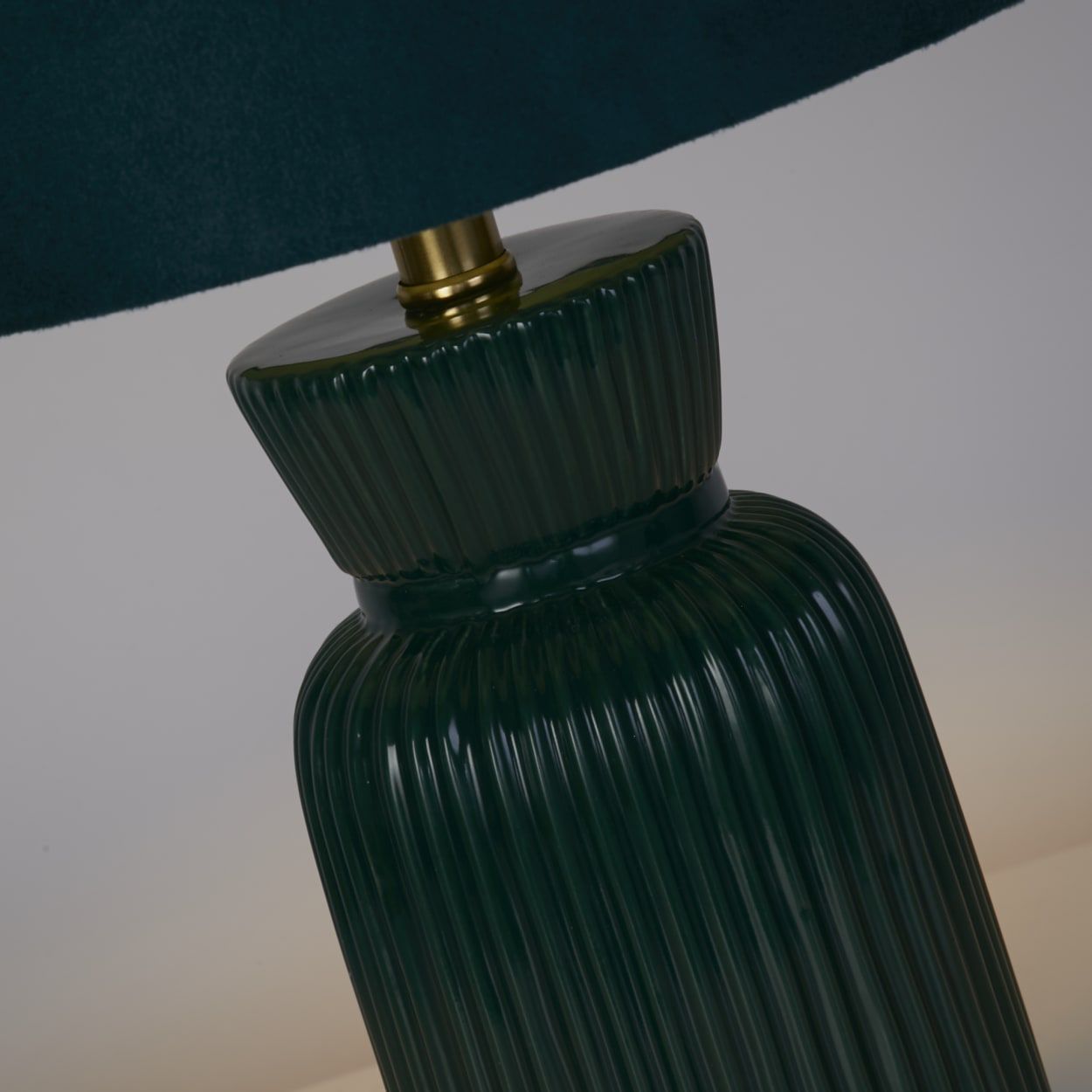 Close up of the Tia emerald table lamp's fluted neck and brass gallery fitting beneath the velvet drum shade