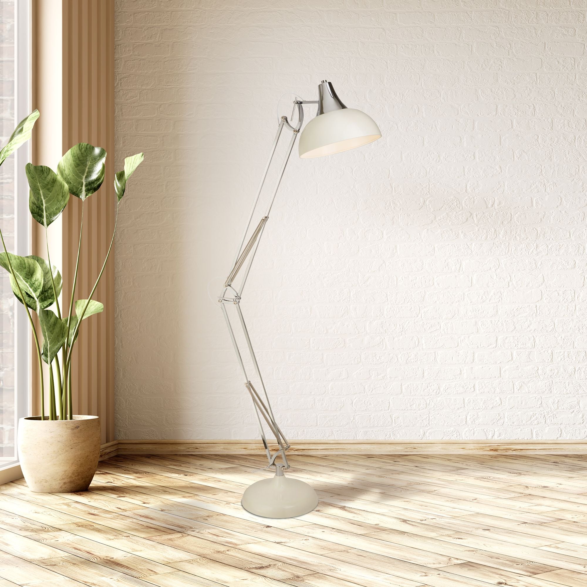 Goliath floor lamp with its arm angled downward, styled beside a potted plant against a whitewashed brick wall