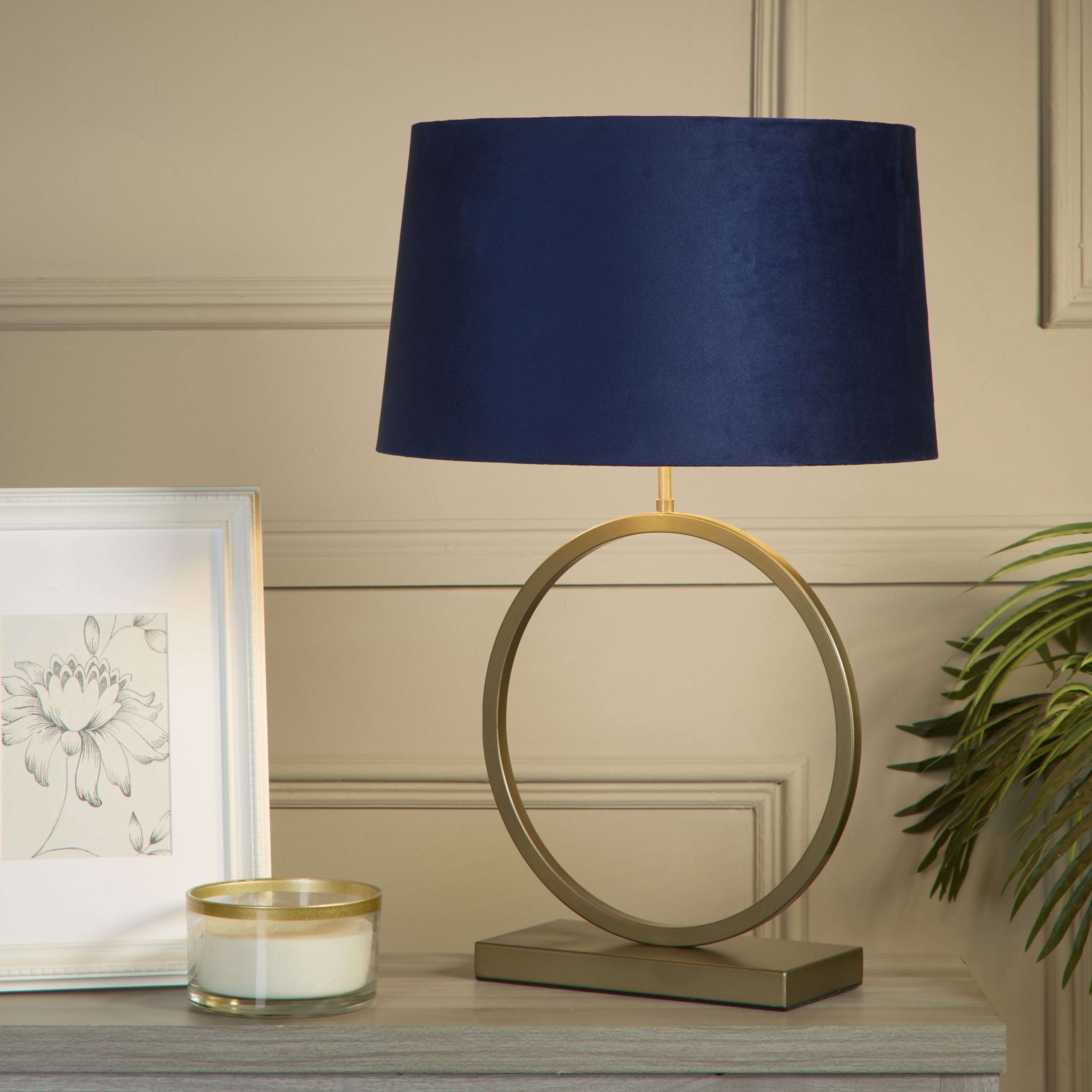 Elegant table lamp with navy velvet shade styled on a console table with a framed botanical print, candle and trailing plant