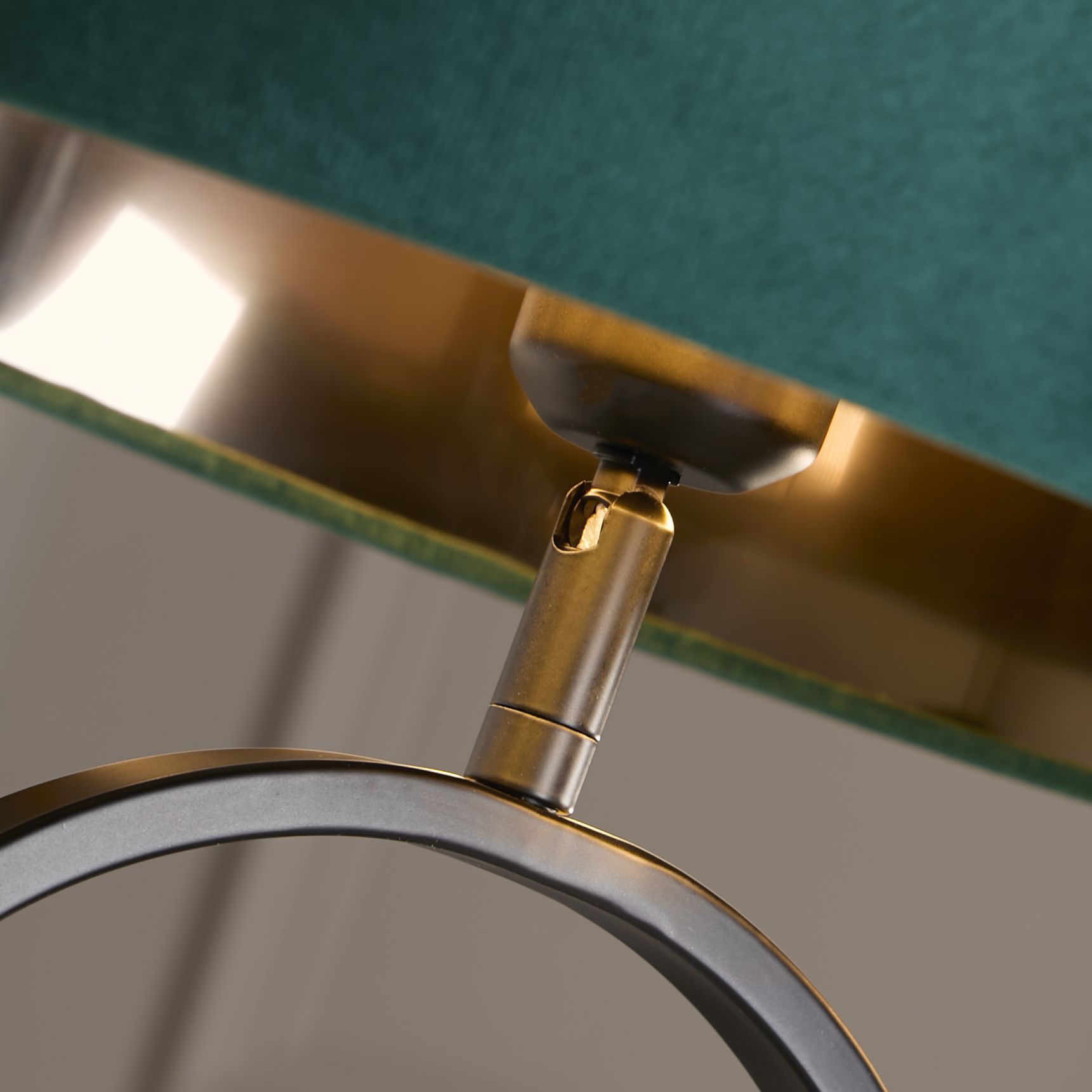 Close up of the brass adjustable joint connecting the emerald velvet shade to the matt black oval base