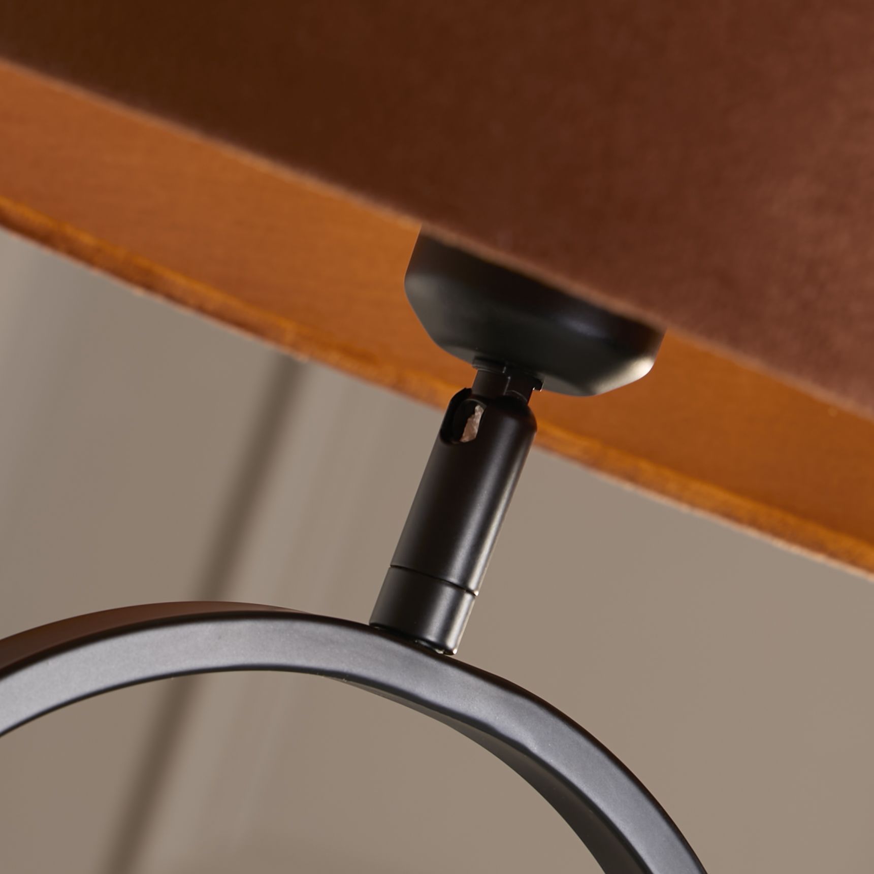 Close up of the brass adjustable joint connecting the burnt orange velvet shade to the matt black oval base