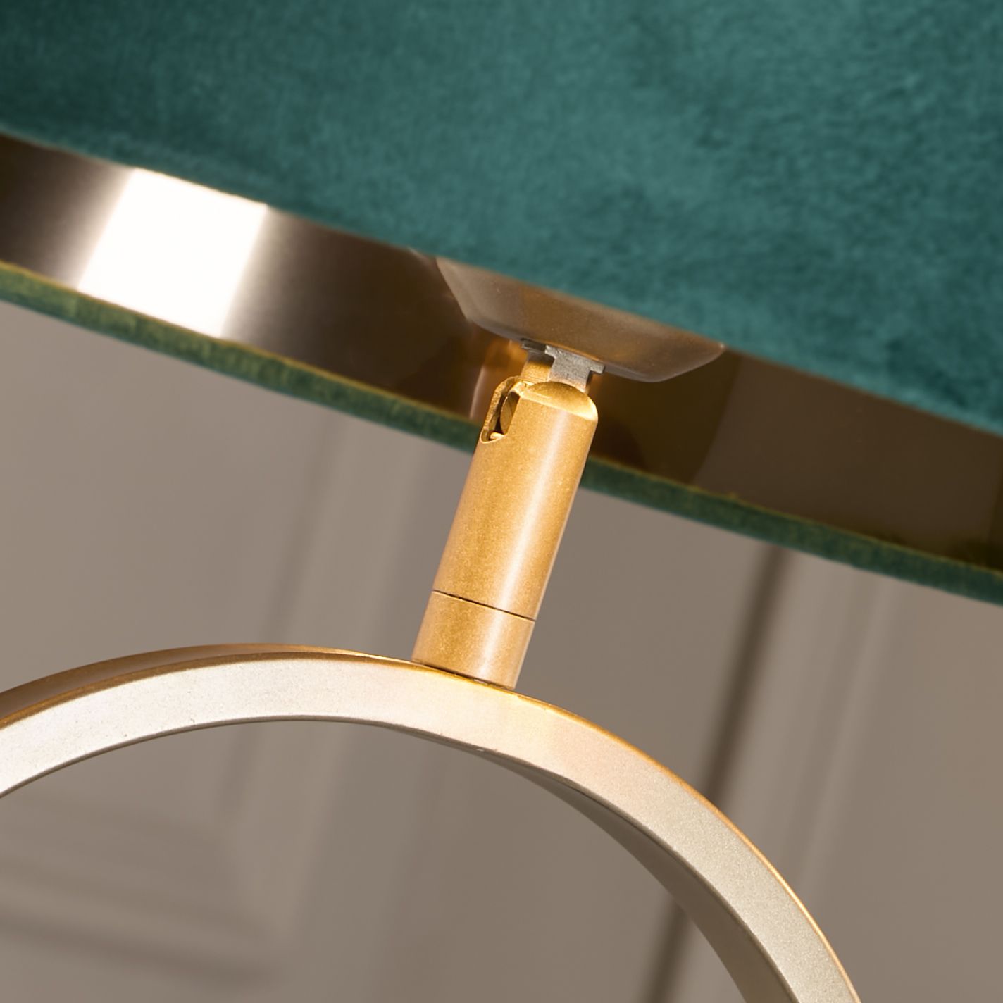 Close up of the bronze table lamp's swivel neck joint, showing where the oval ring base meets the emerald velvet shade