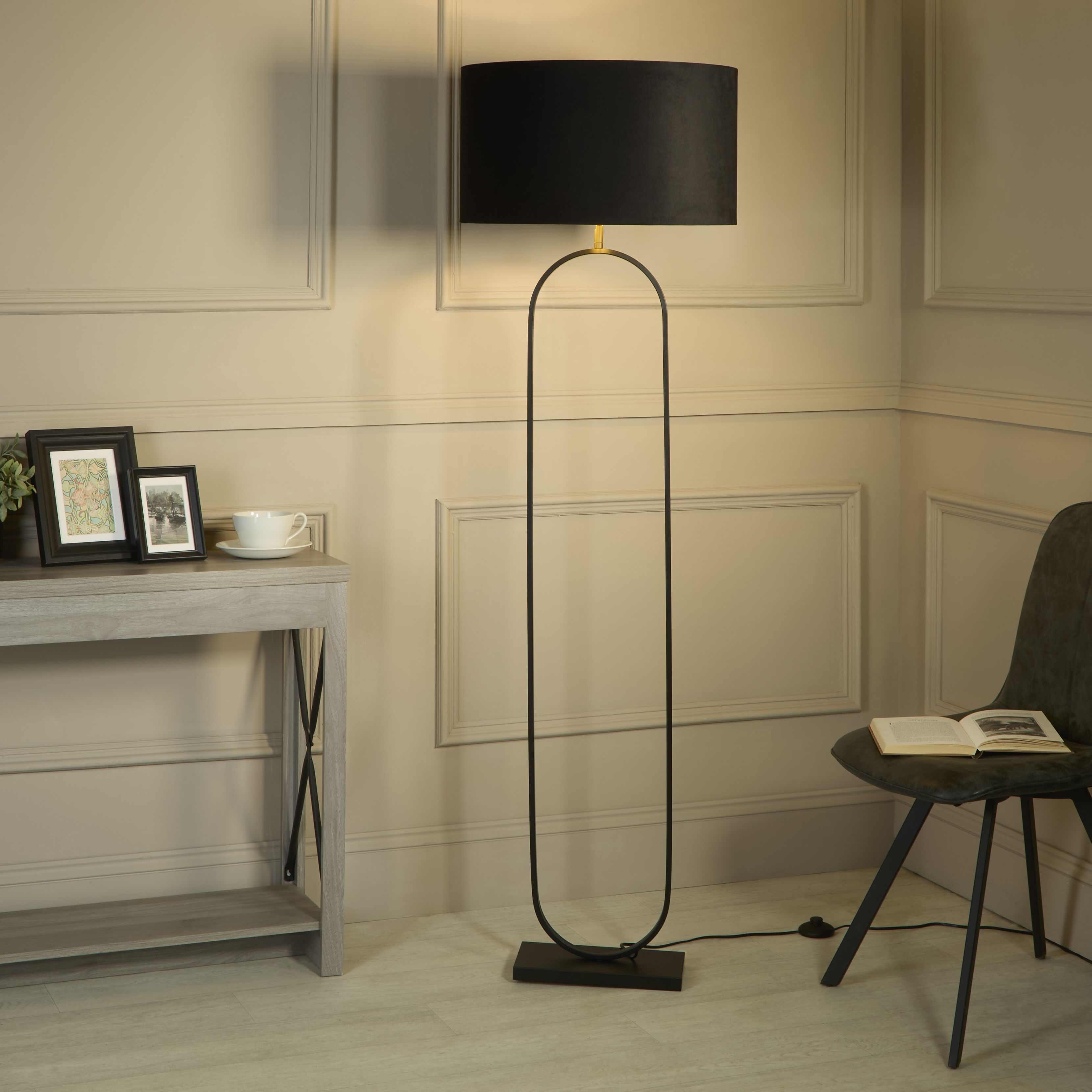 Modish floor lamp with black velvet shade styled in a panelled living room beside a console table and a black armchair