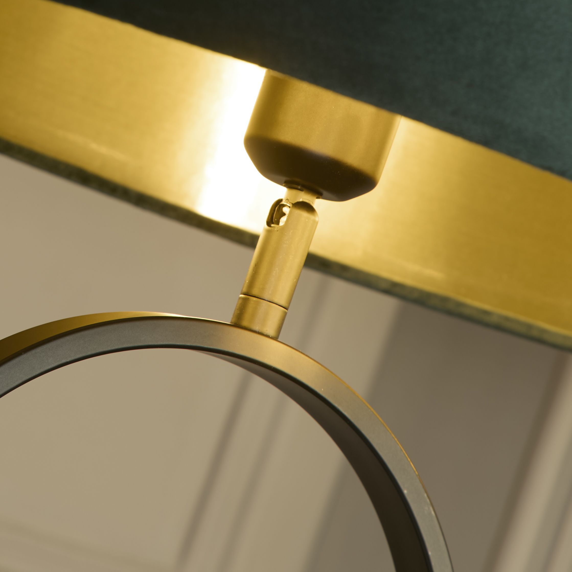 Close up of the brass adjustable joint connecting the green velvet shade to the black oval ring base