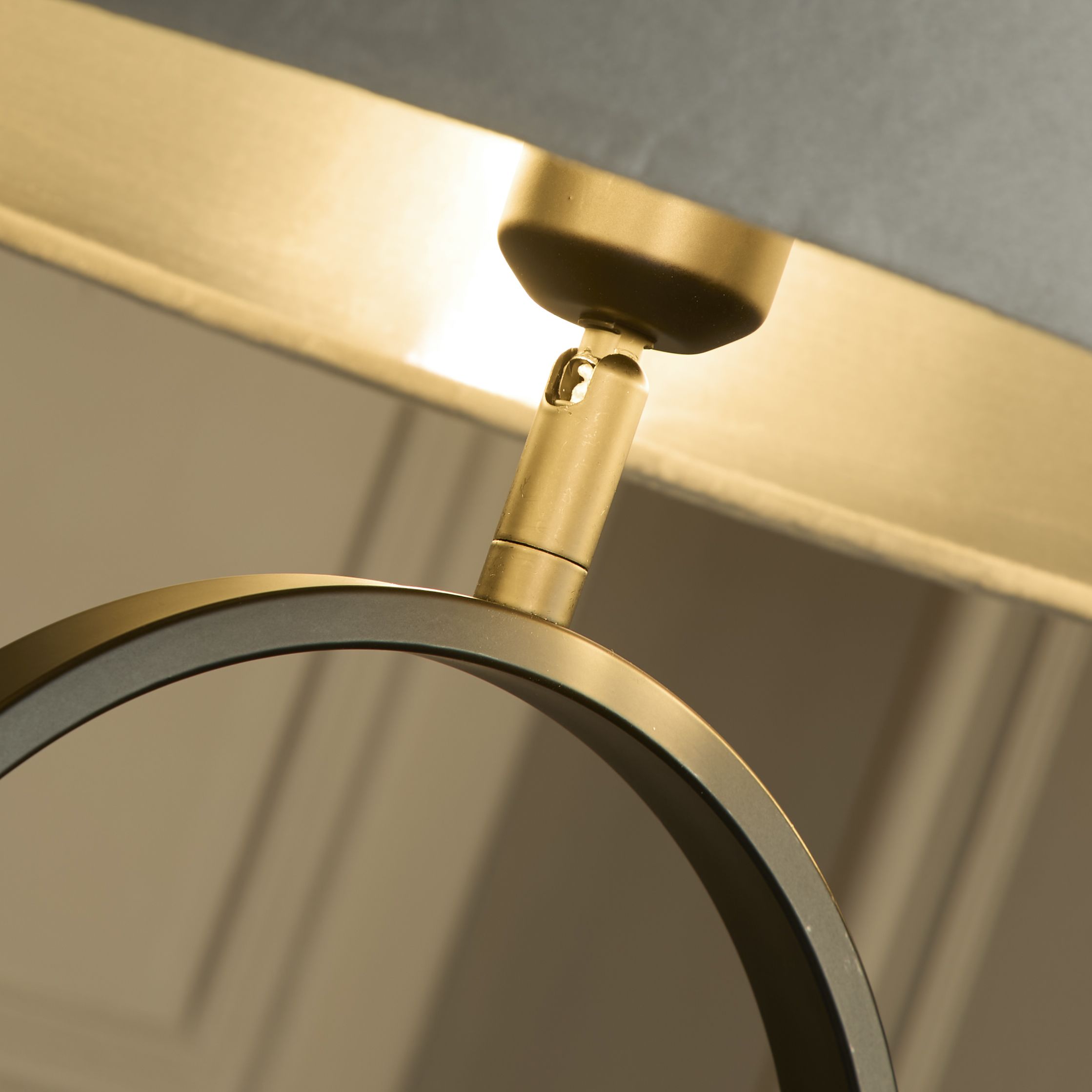 Close up of the brass adjustable joint connecting the light grey velvet shade to the black oval ring base